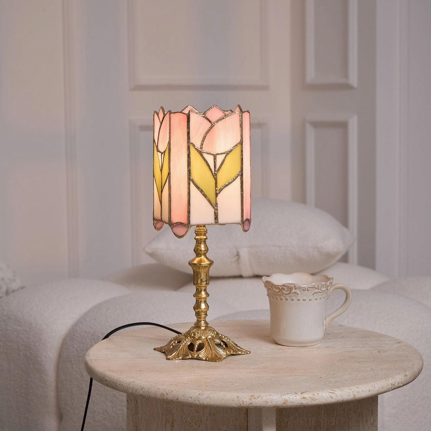 Brass gold tulip glass table lamp on light gray sofa side table with yellow-pink glass shade and ceramic mug