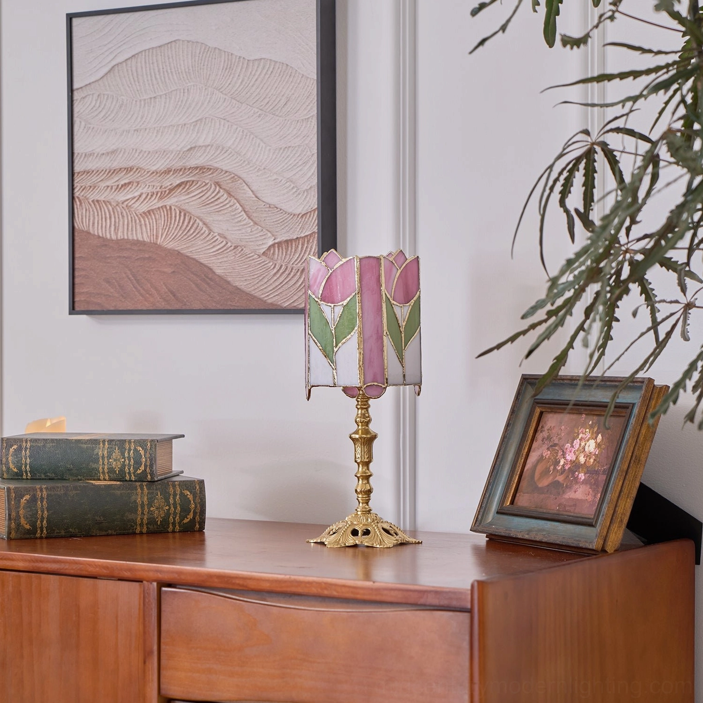 Pink and green tulip stained glass table lamp on wooden dresser with indoor potted plant and landscape wall art