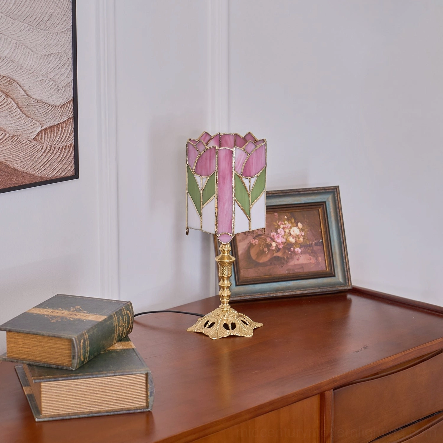 Tiffany tulip lamp three-quarter side view on wooden dresser with stacked vintage books and framed painting