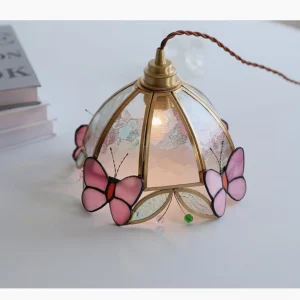 Overhead top-down view of Valinte pendant light displayed on tabletop with stacked design books, showing intricate stained glass butterfly patterns and green glass ornaments
