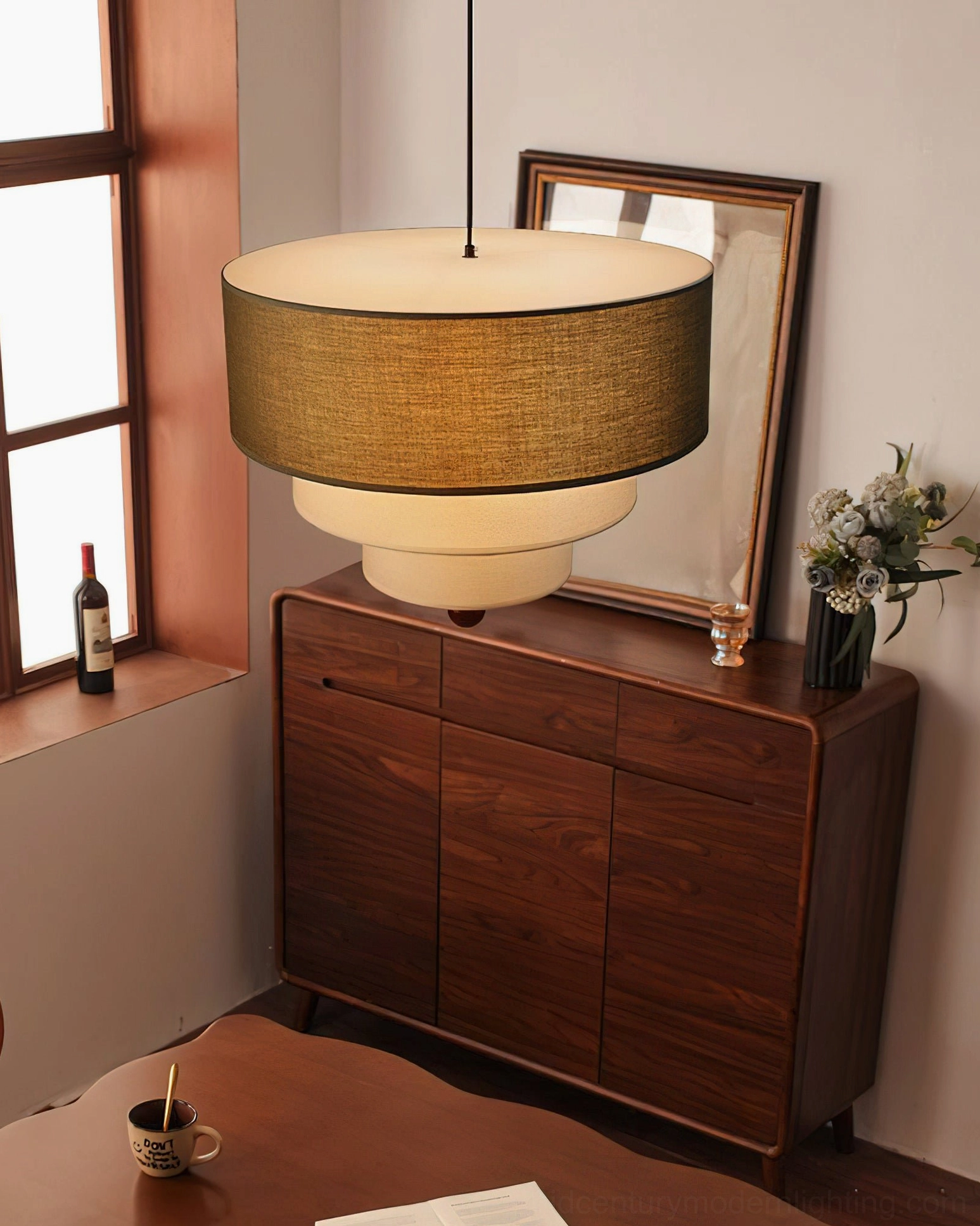 Vanelia mid-century modern pendant lamp installed in dining nook above wooden sideboard, three-quarter angle showing layered fabric construction and metal hardware