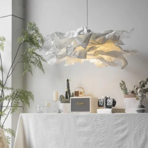 Veli pendant light suspended over minimalist dining table, warm glowing illumination, pleated fabric-like paper shade