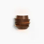 Veneer layered wall lamp frontal studio view with warm backlit glow showcasing tiered wood grain metal design