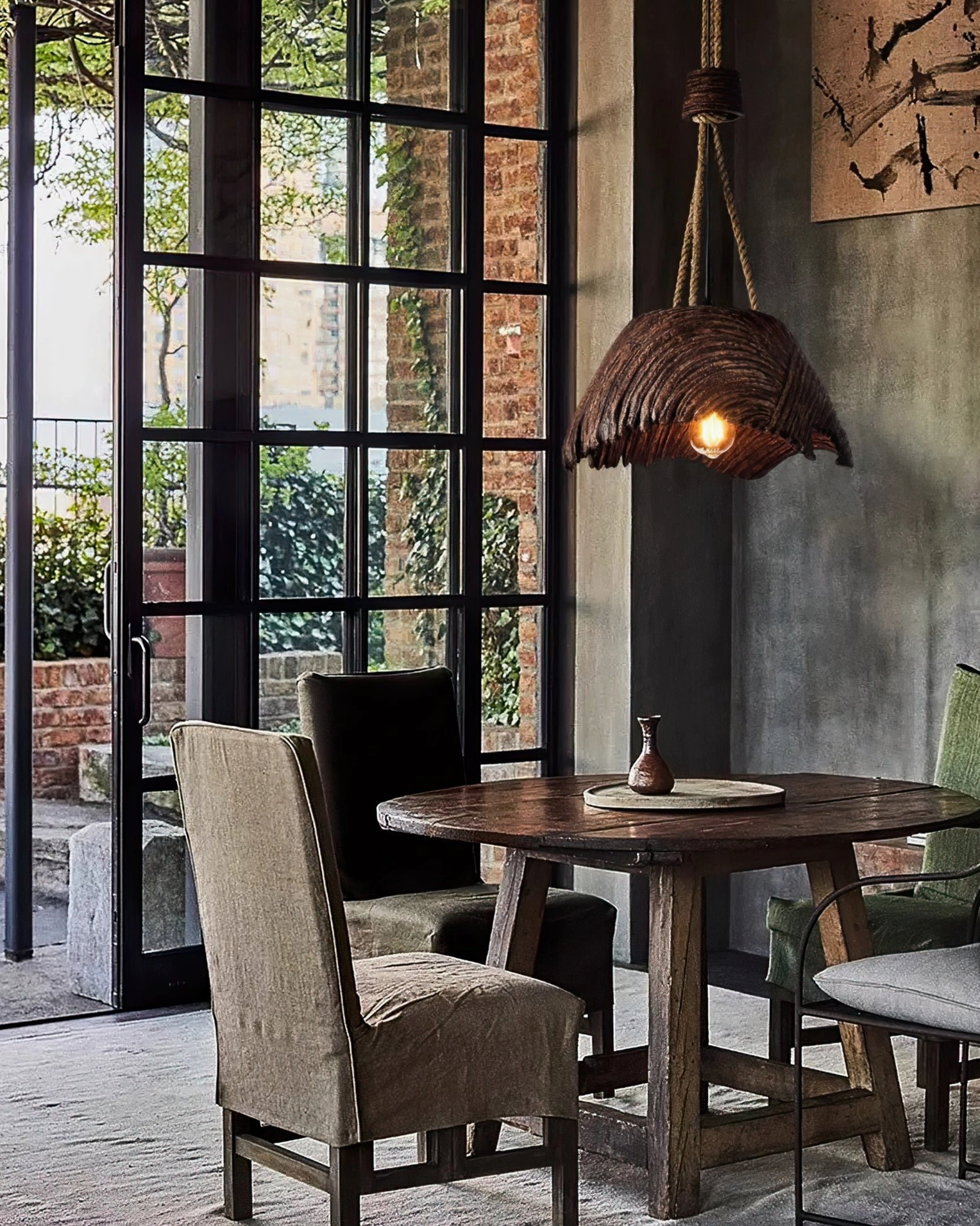 Vintage rope pendant hanging above round wooden dining table in rustic dining area with floor-to-ceiling windows