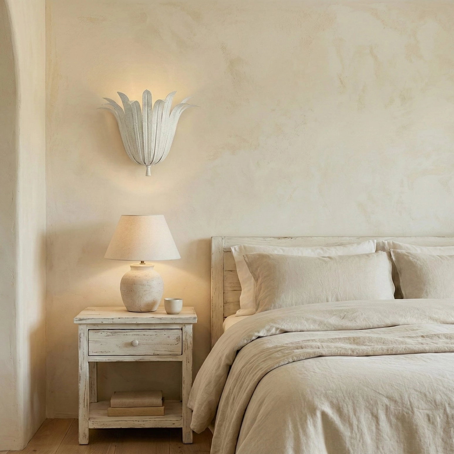Off-white Vicenzio leaf sconce mounted in quiet minimalist bedroom with white wooden nightstand and neutral linen decor