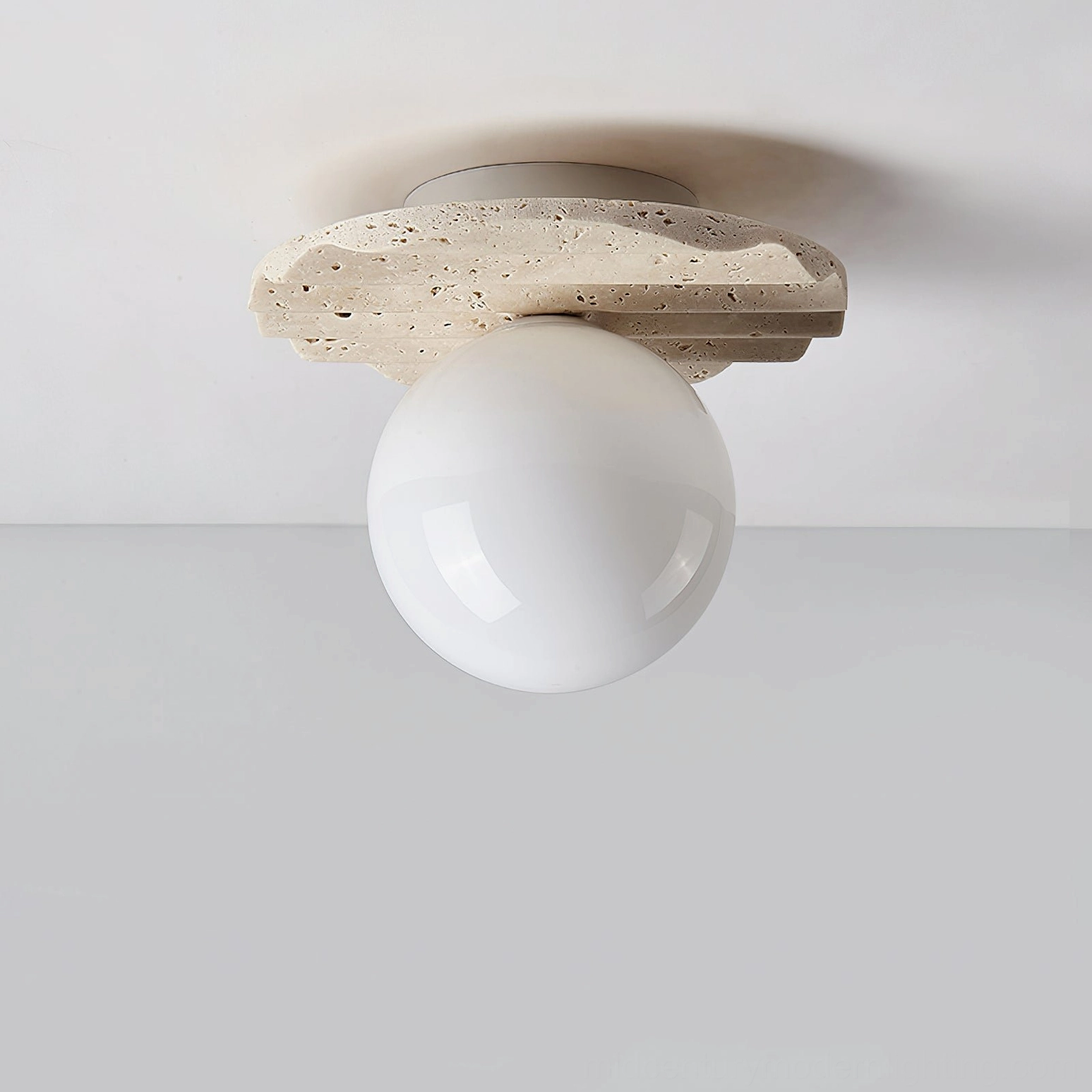 Victor pendant light fixture three-quarter view, unlit, showcasing travertine stone base with porous texture and natural color variation, glass diffuser globe