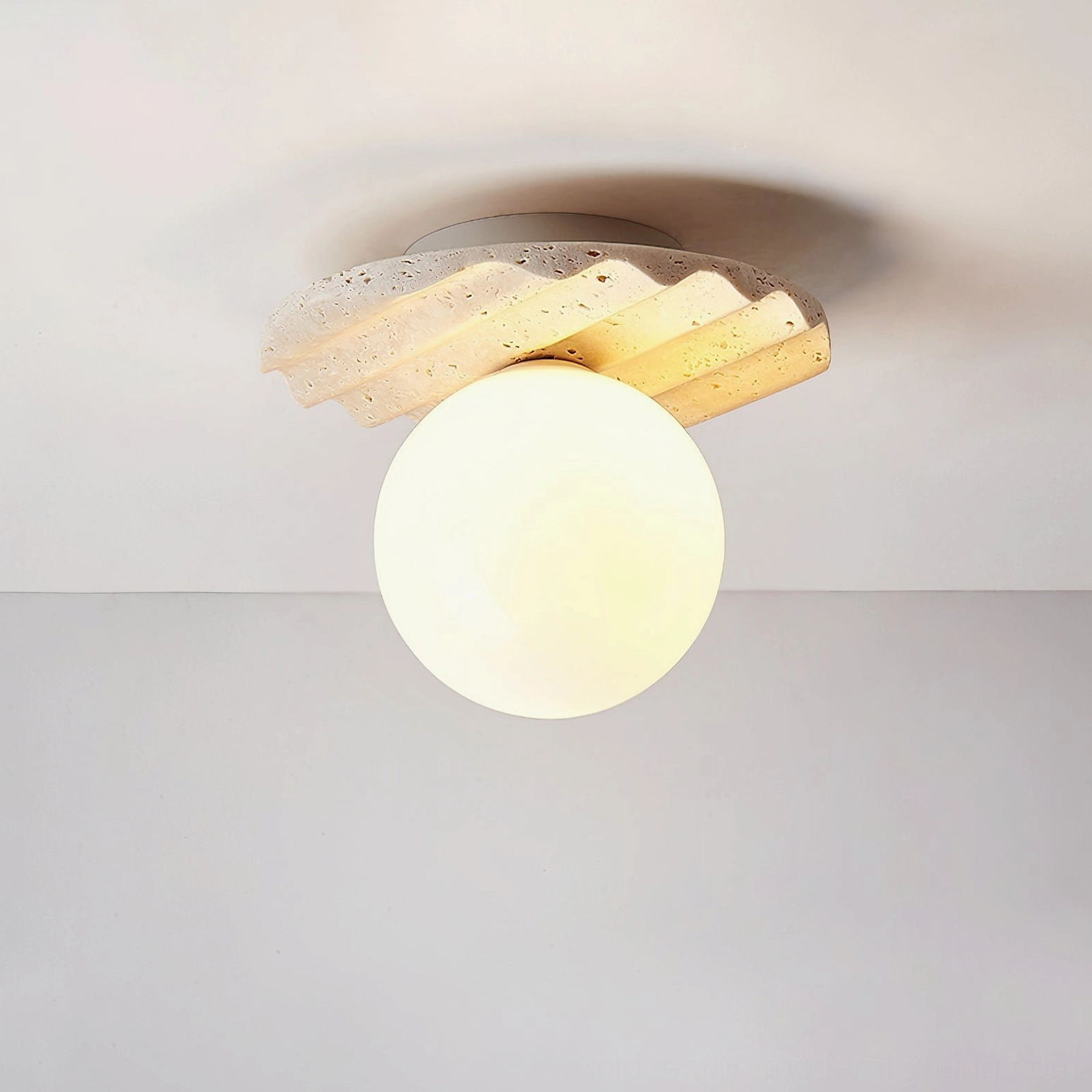 Victor ceiling light illuminated, warm glow emanating from opal glass, travertine base with visible fluting details, soft light diffusion overhead view