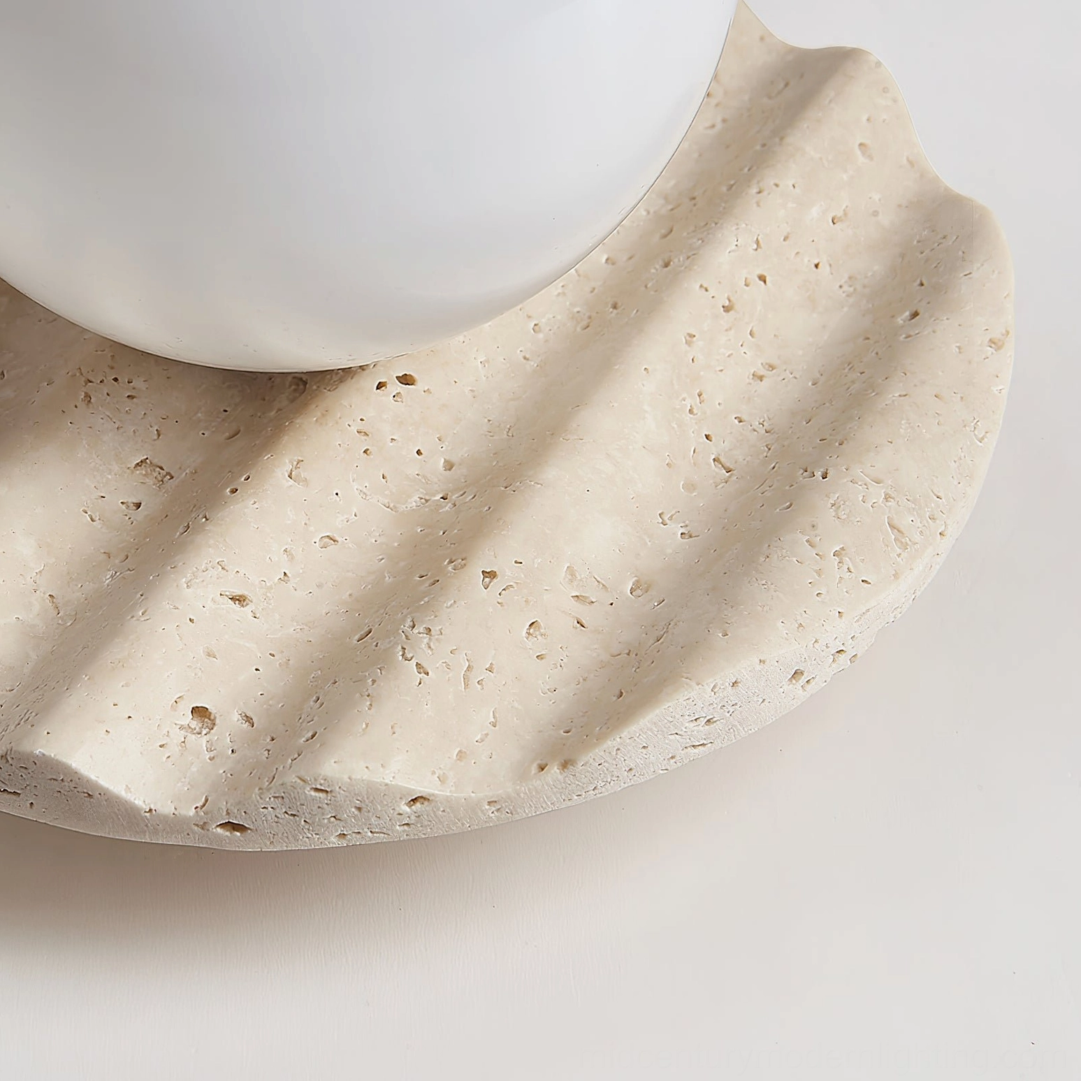 Close-up macro detail of Victor travertine base, showing natural porous stone surface, fluted scalloped sculpting, and partial view of opal glass bulb element
