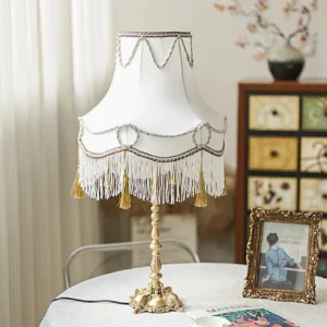 Ornate Victorian brass carved base lamp with fringed fabric shade on home tabletop