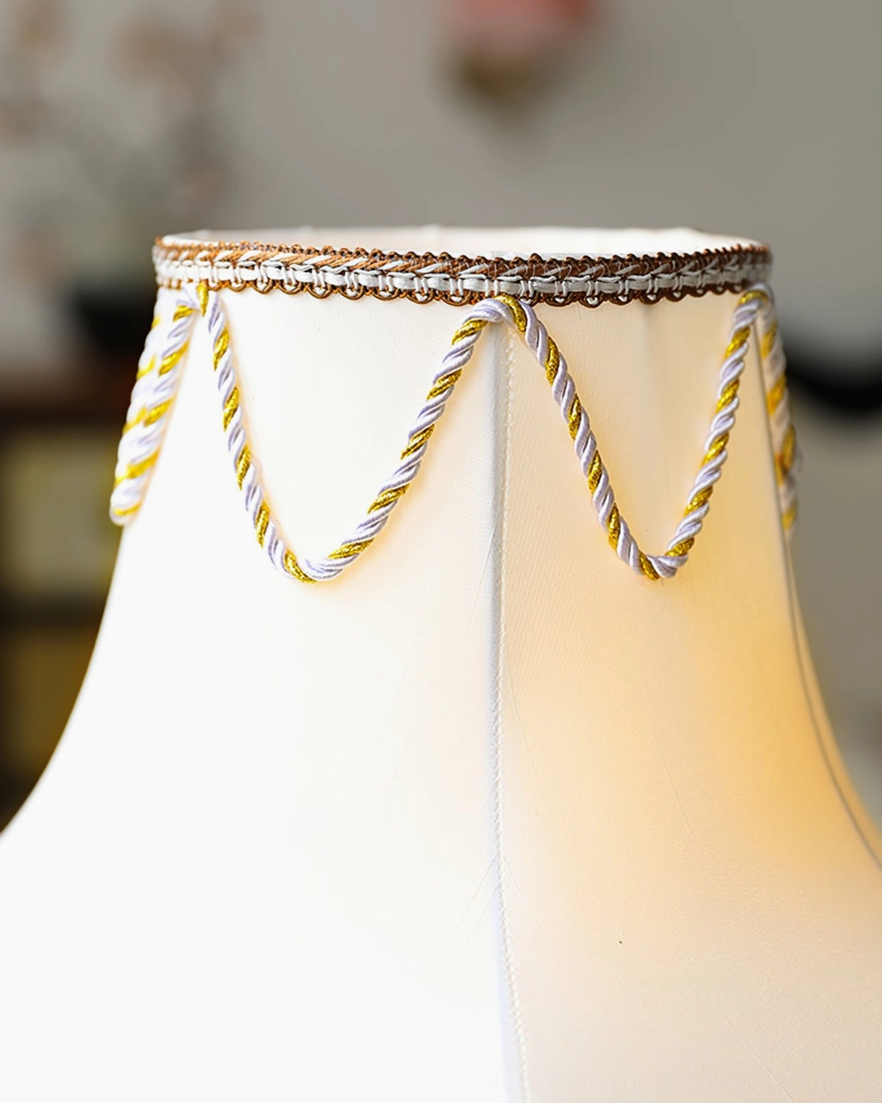 Illuminated Victorian brass table lamp with glowing white fabric shade and gold twisted trim
