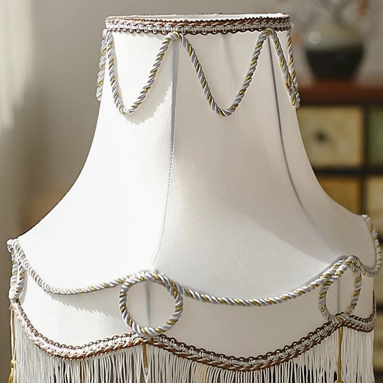 Close-up detail of white fabric lampshade with braided gold trim and tassel fringe