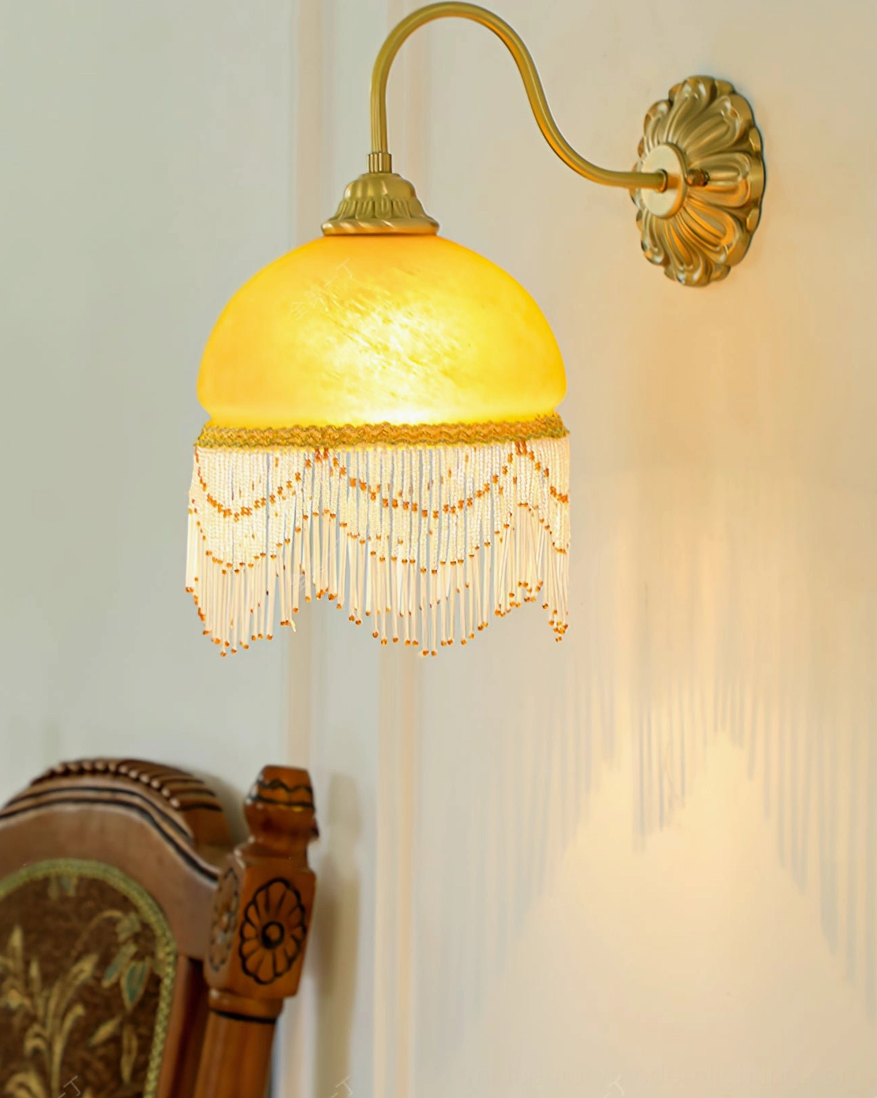 Vili wall lamp illuminated in corner with vintage wooden chair, gentle warm glow and delicate tassel trim creating vintage ambiance