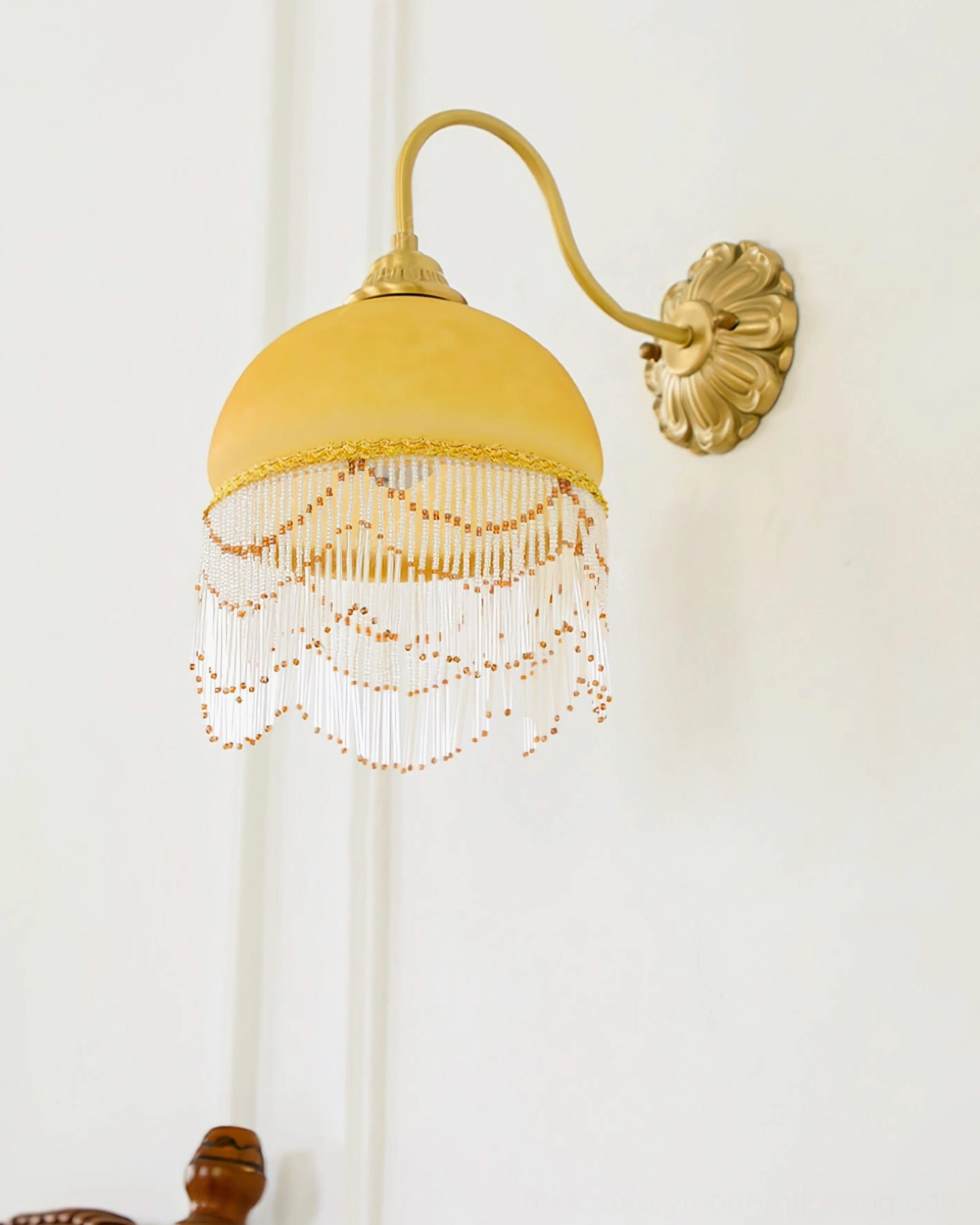 Unlit Vili wall lamp on bright indoor wall background, showcasing milky yellow shade and beaded fringe decoration