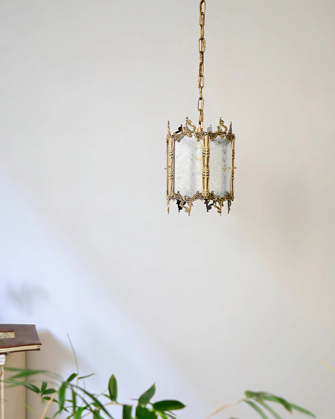 Vintage brass lantern pendant fixture in compact retro design with subtle green plant accents against plain white wall