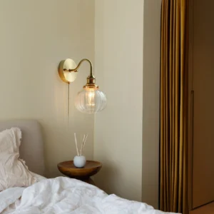 Brass wall lamp mounted bedside with warm Edison bulb glow - cozy bedroom mid-century lighting setup