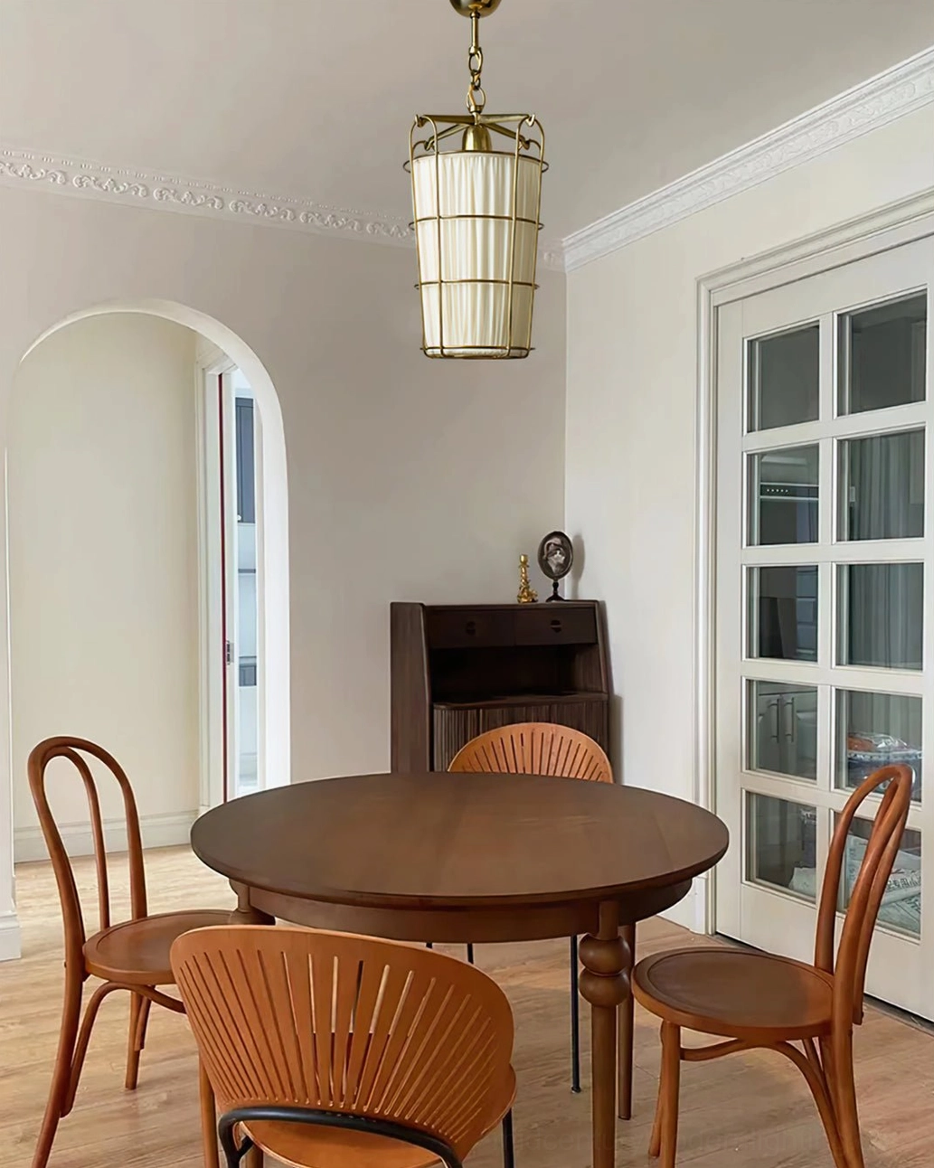 Retro dining room installation with caged pendant above wooden round table, arched doors visible