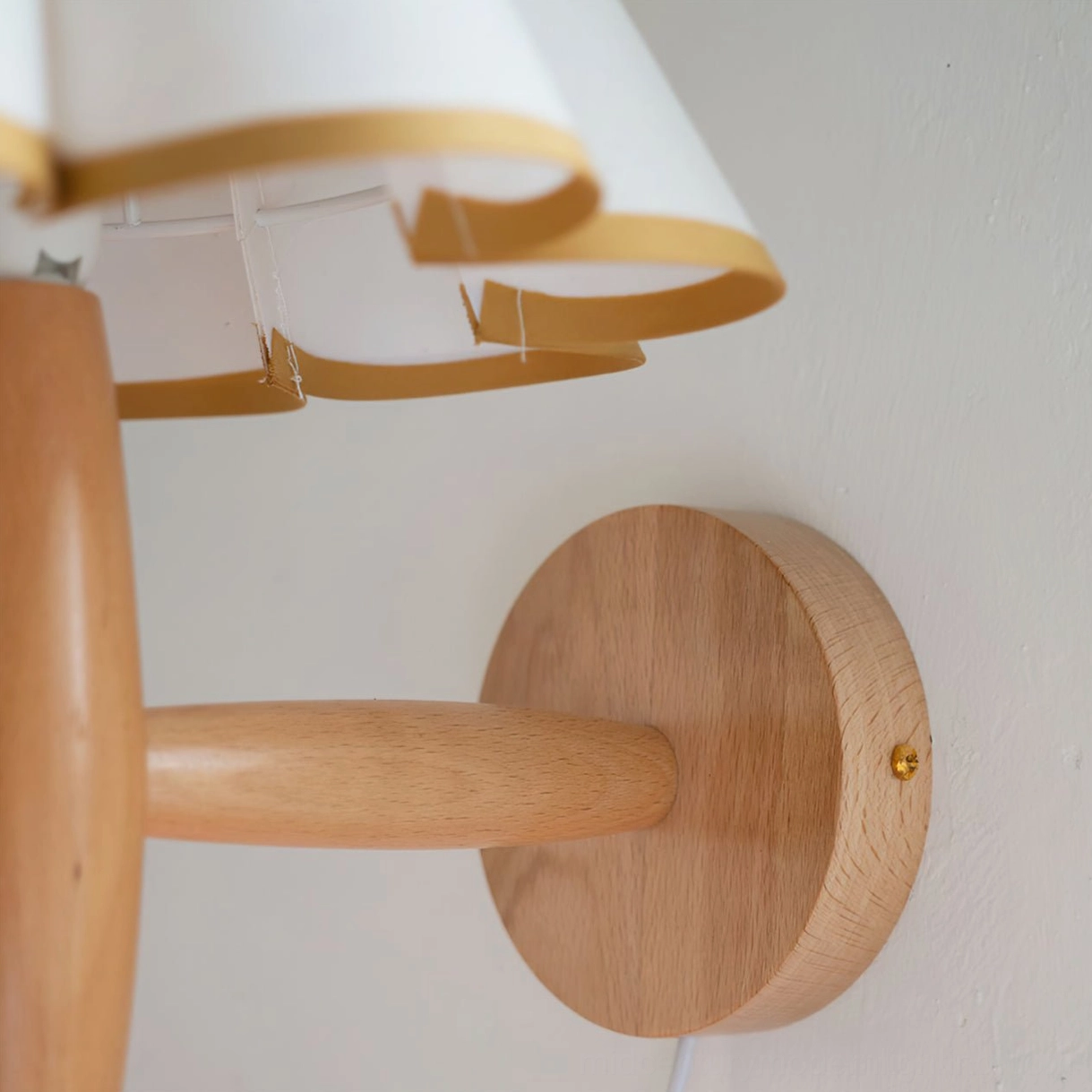 Fluted wall lamp detail showing natural wood backplate and pleated fabric edges with gold trim