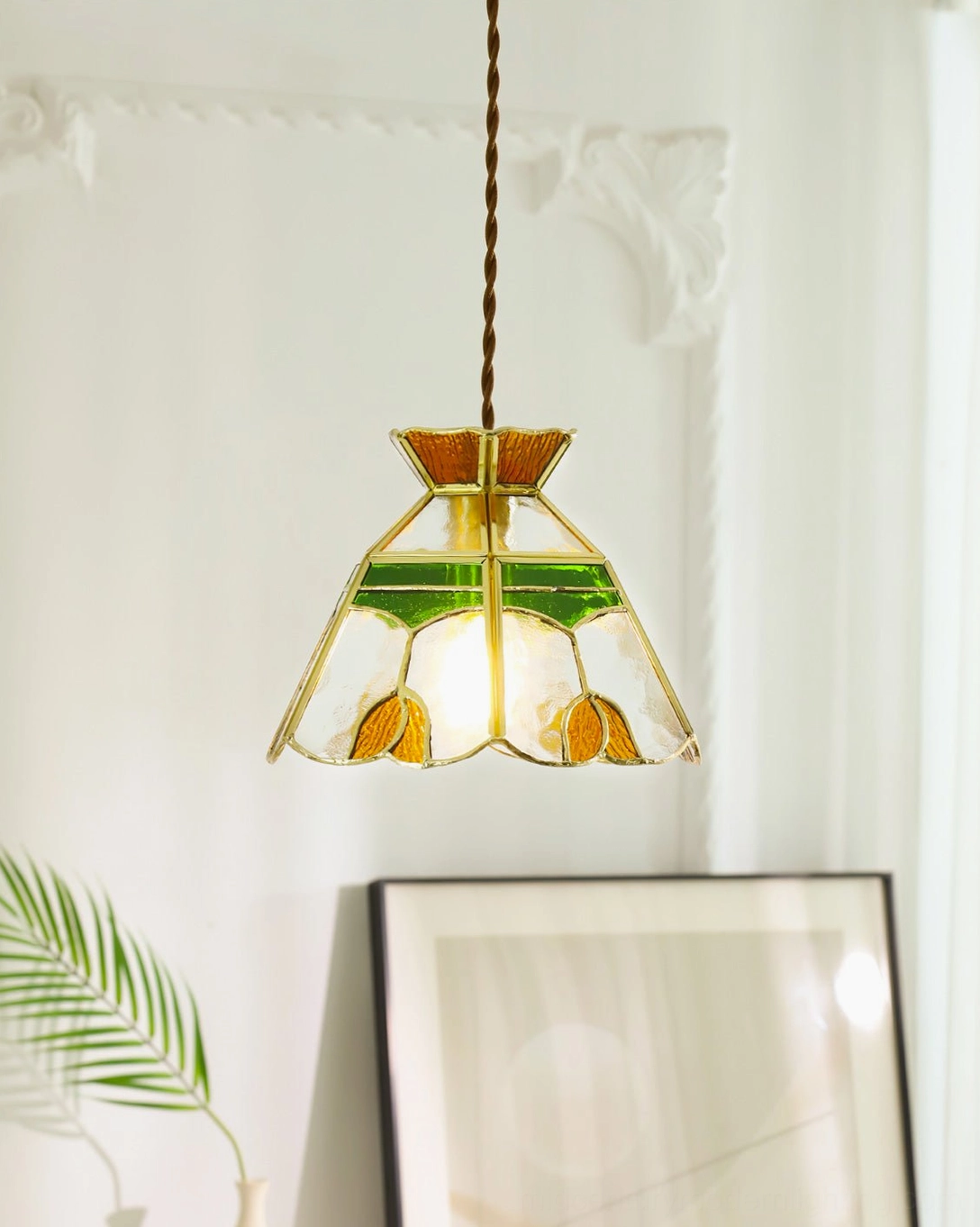 Vitral stained glass pendant hanging against indoor wall with framed artwork and twisted cord
