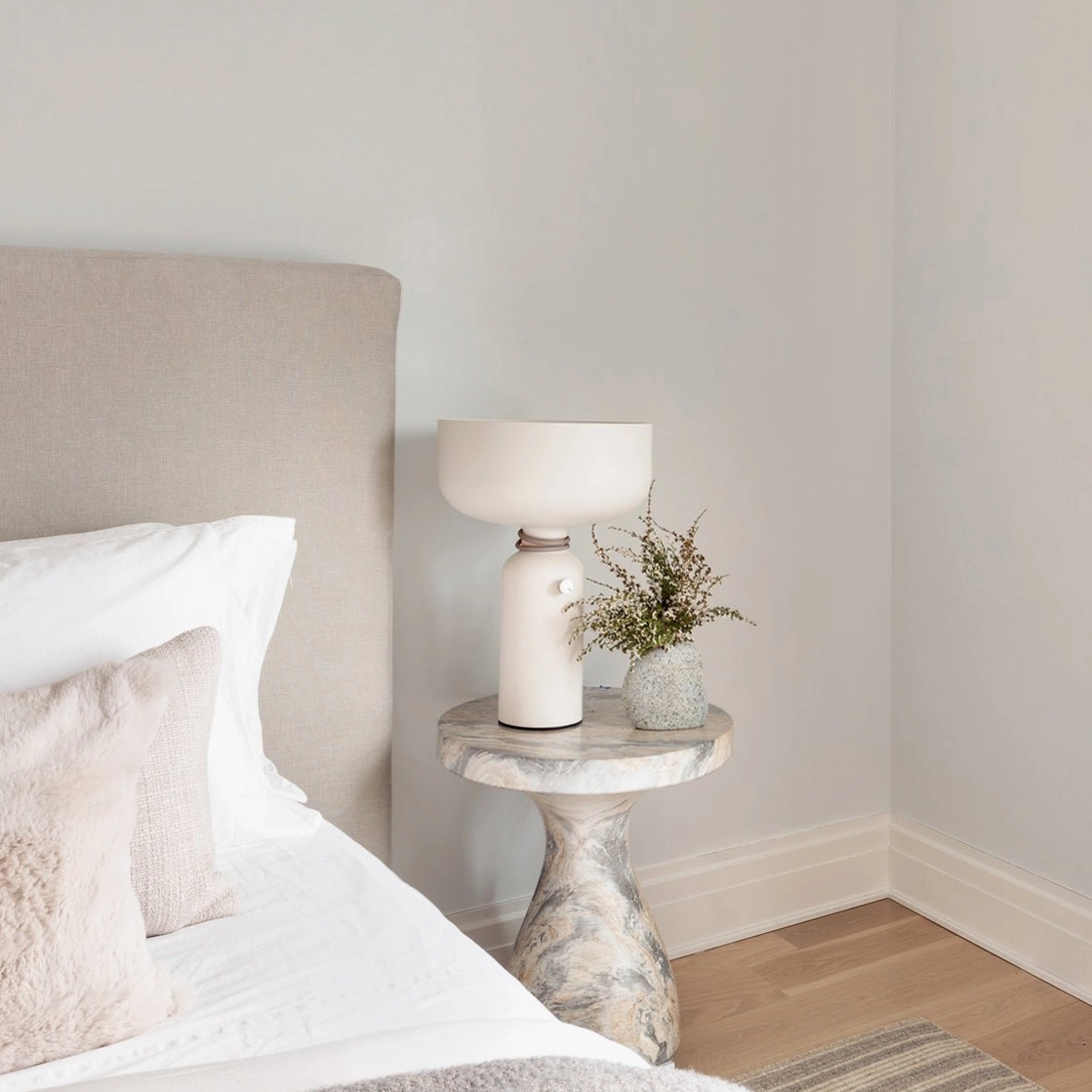 Vol off-white table lamp on marble nightstand in cozy bedroom with potted plant decor