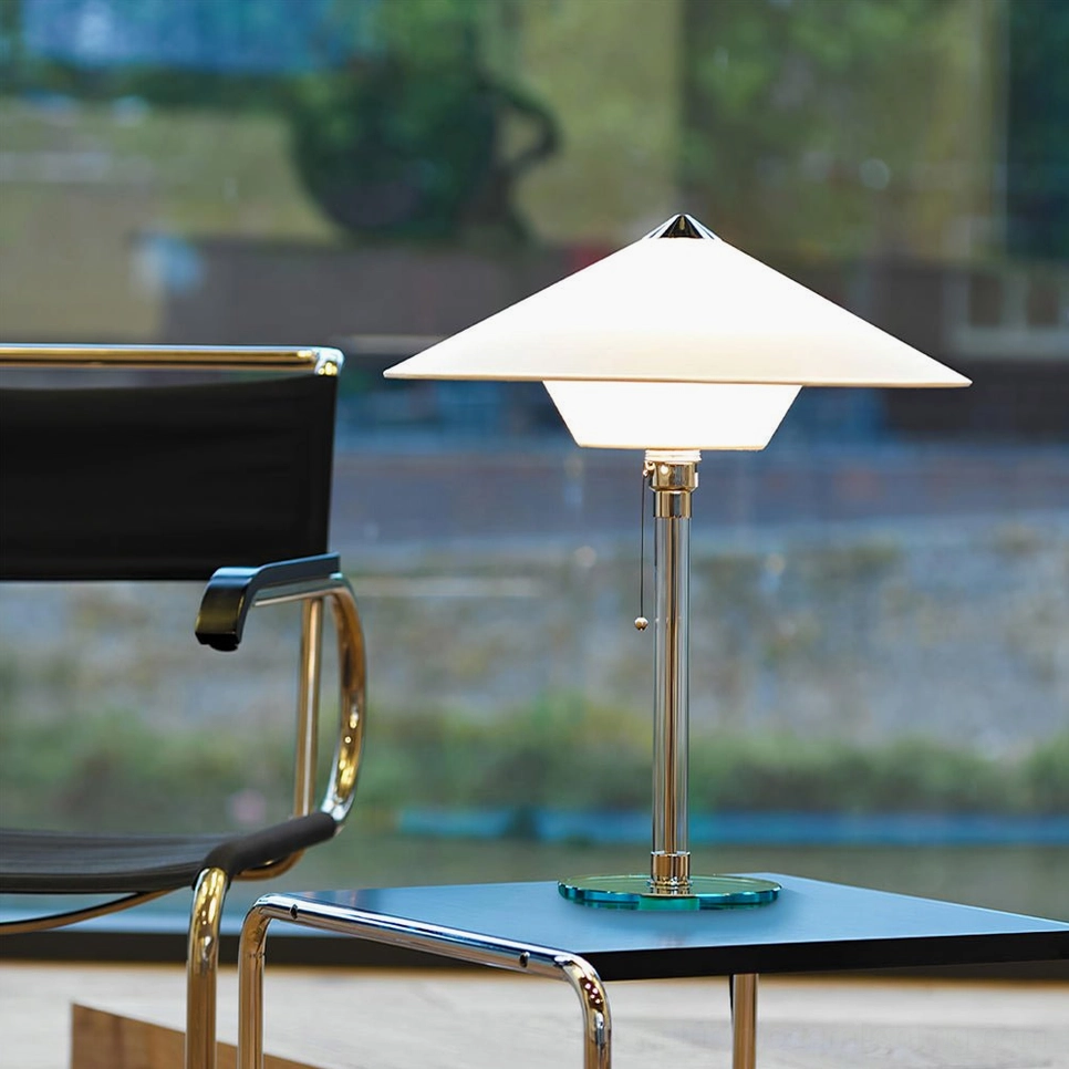 Mid-century modern Wagenfeld table lamp positioned on side table in contemporary office lounge with leather chair
