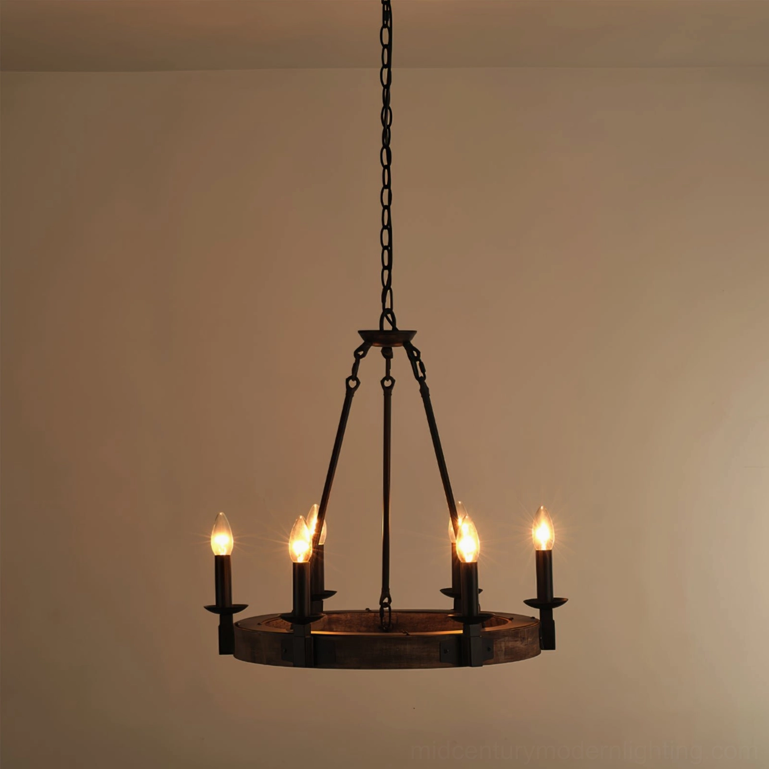 Front distant view of wagon wheel chandelier with four lit candle bulbs creating warm glowing ambient light in beige interior space