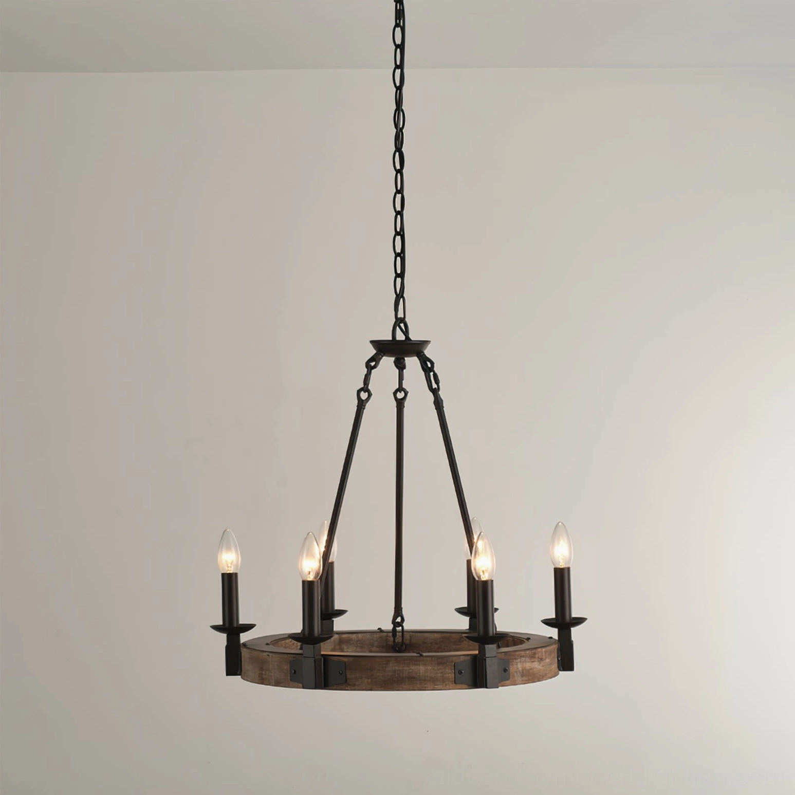 Industrial rustic wagon wheel chandelier mounted from ceiling chain, four lit candle bulbs glowing warm amber light against neutral wall