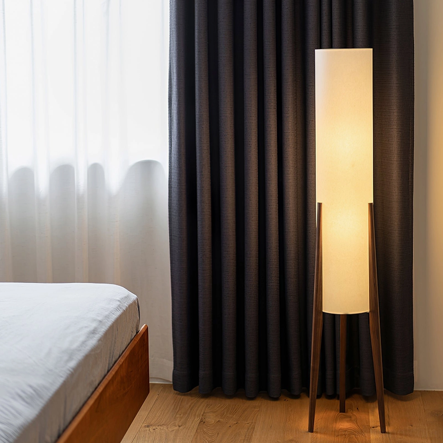Wooden tripod floor lamp in modern bedroom with dark curtains and warm rustic decor