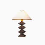 Walnut stacked wood tower table lamp with cream fabric shade and gold trim, studio white background