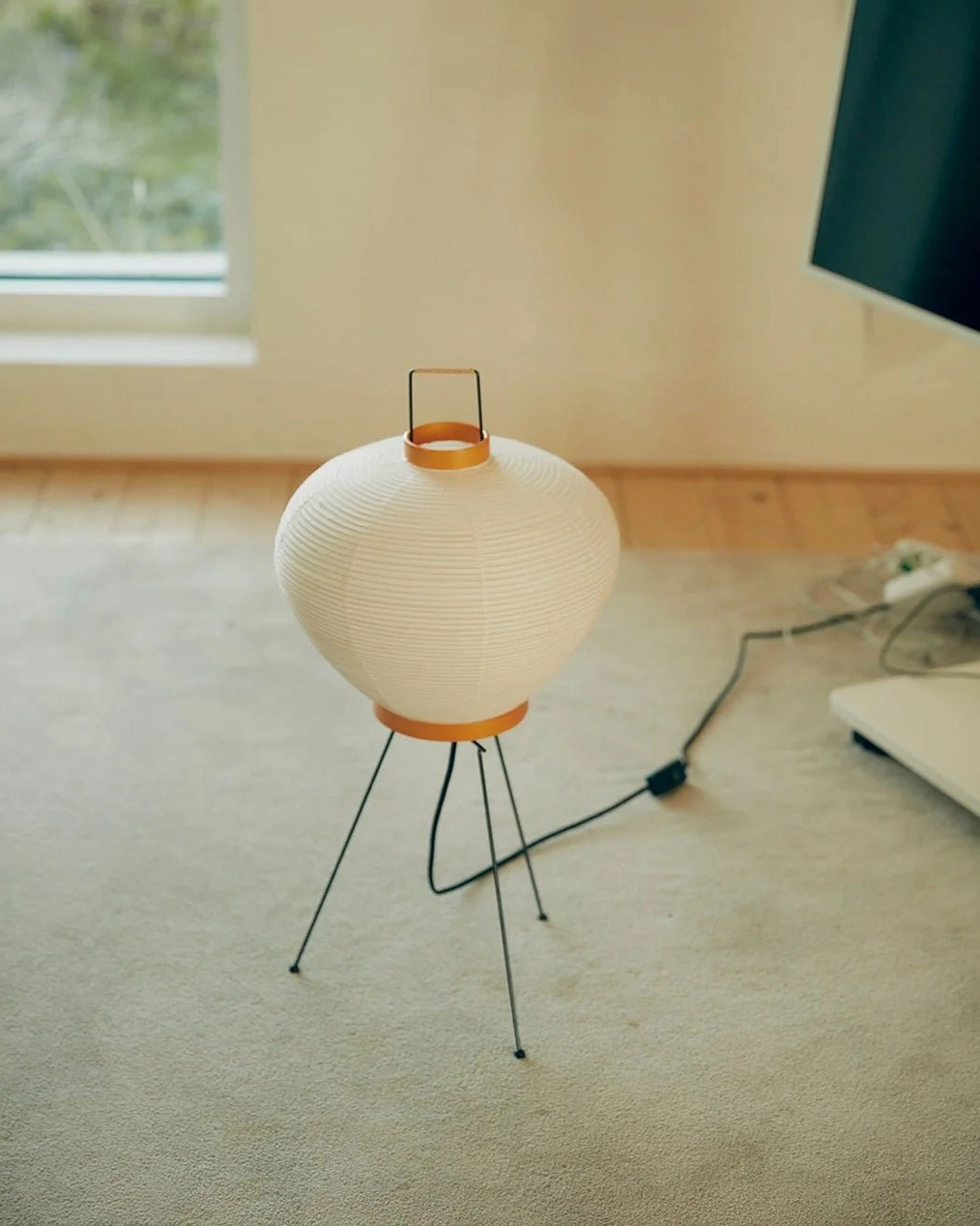 Washi minimalist tripod table lamp on wooden floor in residential room with exposed cord