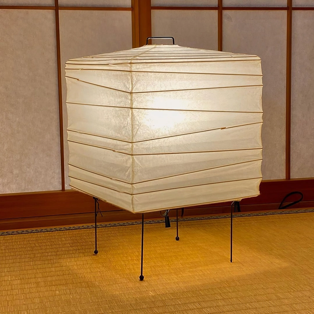 Oversized organic paper table lamp in traditional Japanese tatami room setting, casting warm floor-level accent lighting with soft glow through perforated shade
