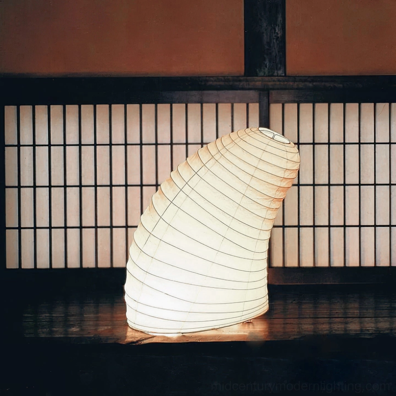Soft warm rice paper table lamp in Japanese-style interior with grille windows, three-quarter side angle showing gentle light diffusion through organic paper