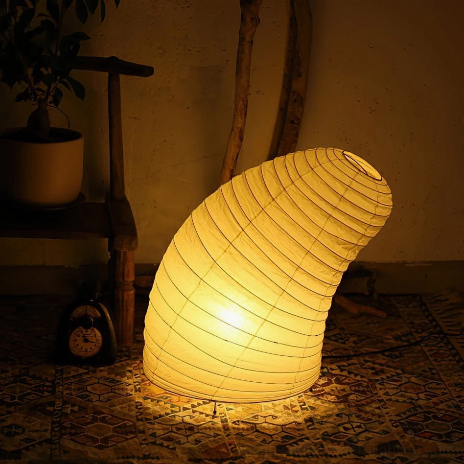 Warm yellow glowing washi paper table lamp in cozy rustic indoor corner, side three-quarter perspective showing ambient light quality