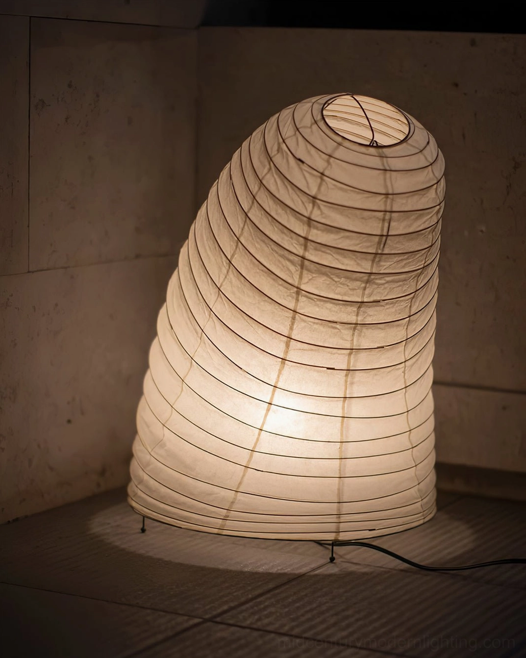 Neutral tone ribbed washi paper table lamp photographed against concrete wall background, front three-quarter angle showcasing sculptural form