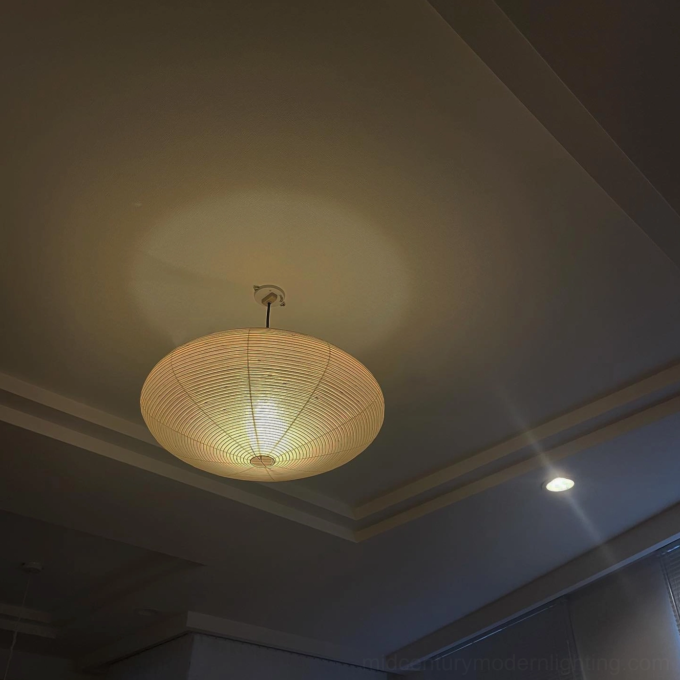Overhead view of washi paper pendant emitting soft warm ambient light in ceiling space, drum silhouette from above