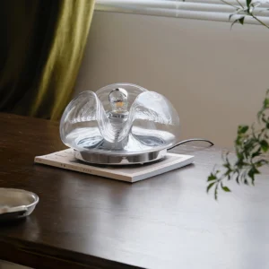 Mid-century wave table lamp on dark wooden dining table with green curtains, side angle view
