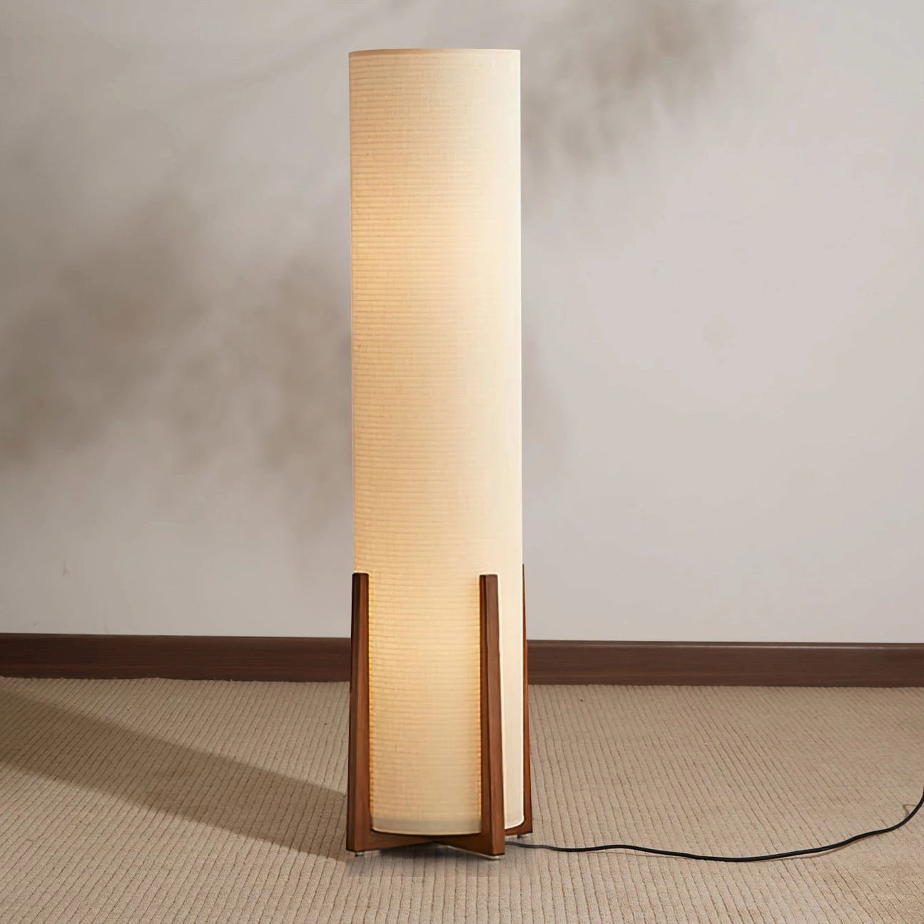 Weave Natural floor lamp producing soft warm light in carpeted room with extended black power cord visible