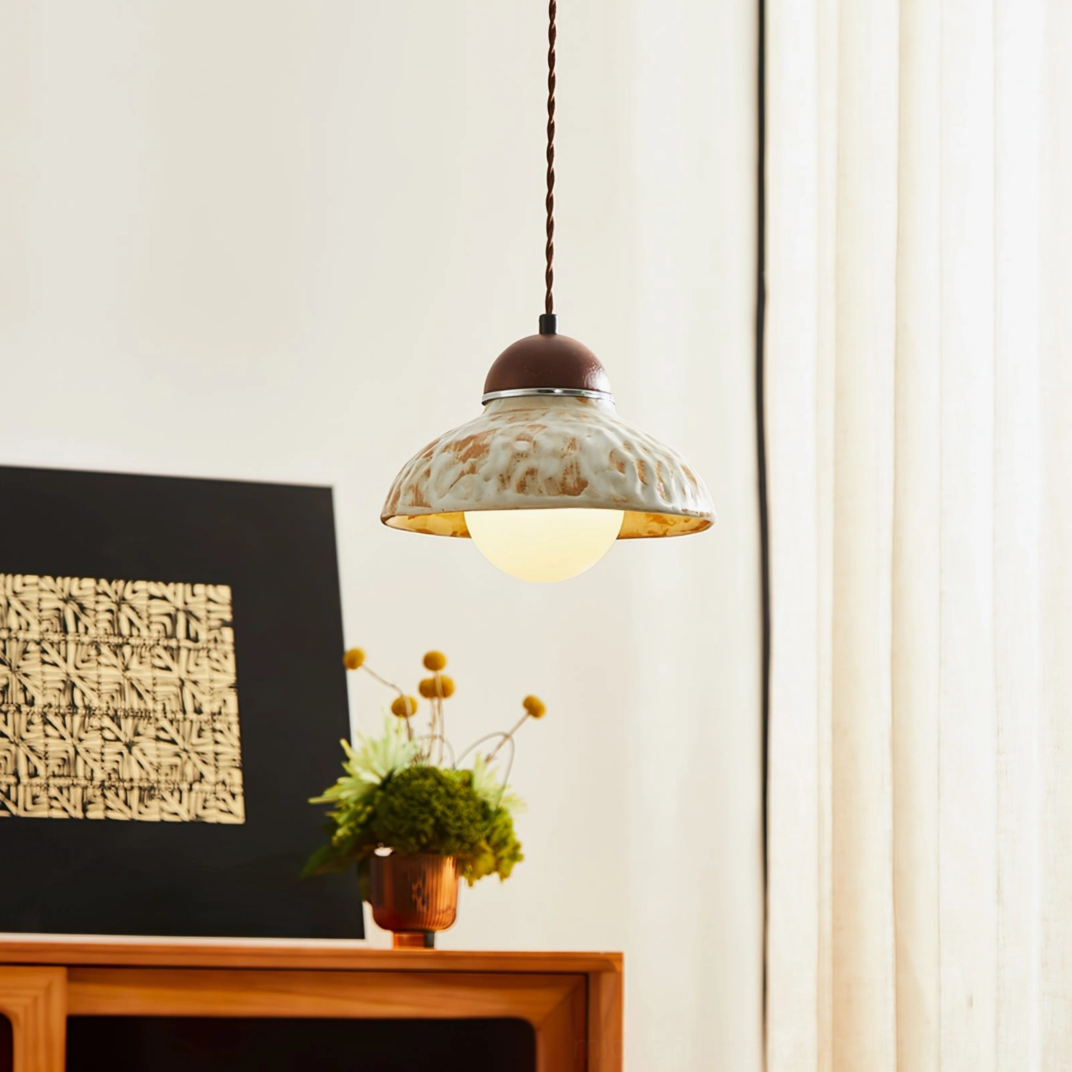Wella ceramic pendant emitting warm light in home corner with decorative artwork and potted plants