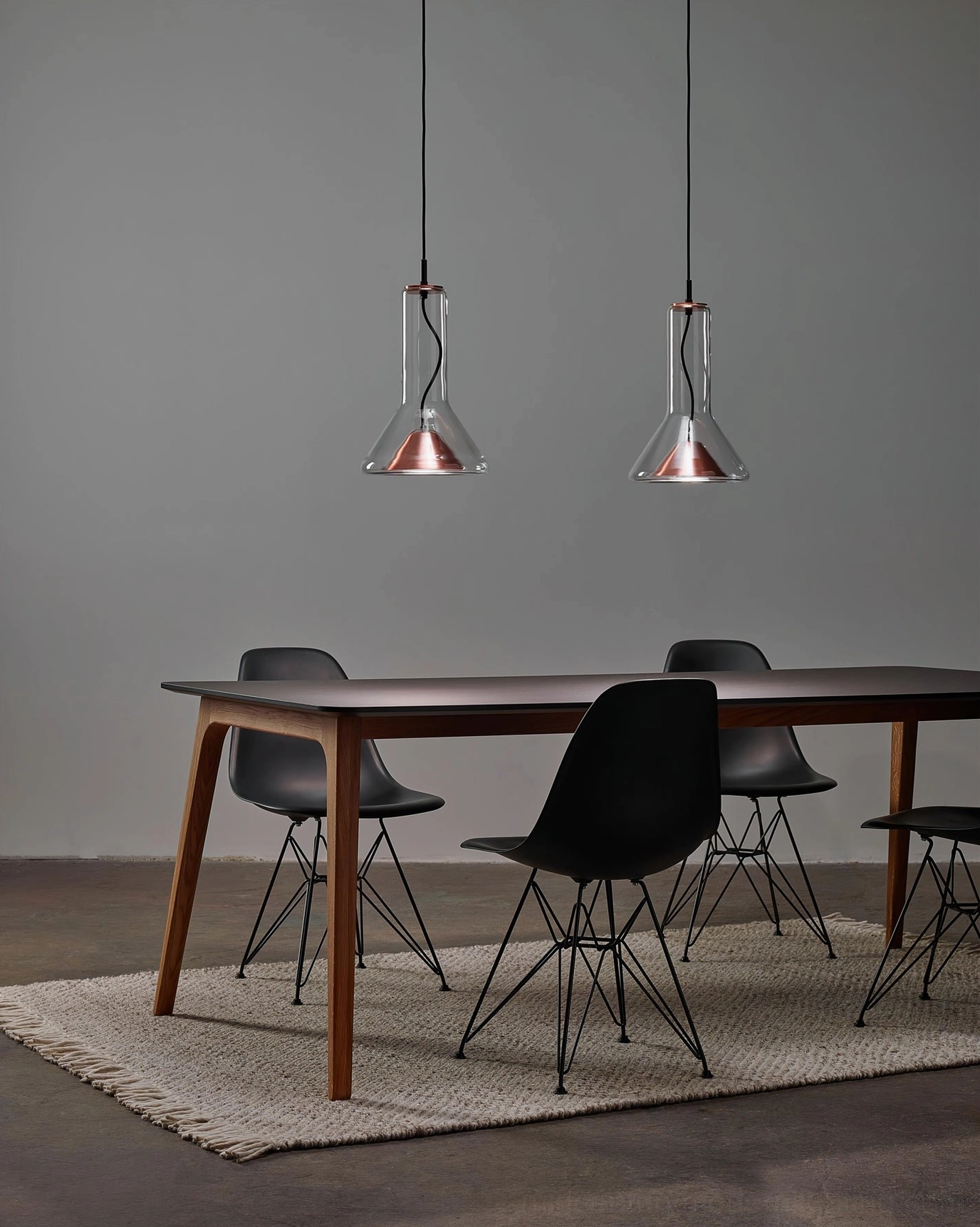 Two copper-trim whistle pendant lamps in modern dining space with wooden table and black chairs