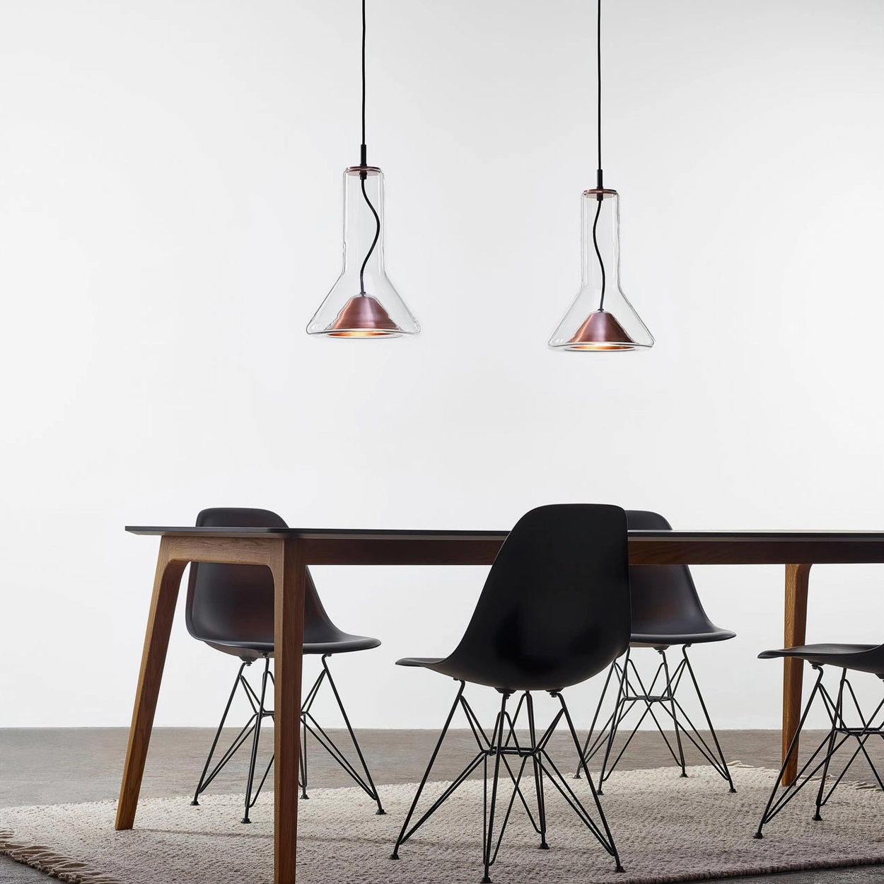 Pair of copper-trim glass pendant lamps hanging above modern wooden dining table, Nordic minimalist decor
