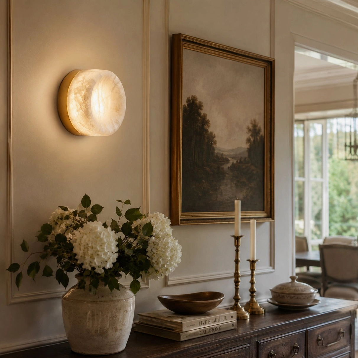 Cream alabaster sconce mounted in formal entryway beside vintage oil painting and hydrangea floral arrangement on side table