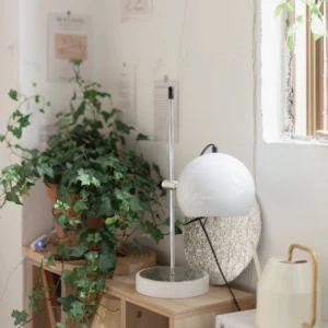 Modern white spherical table lamp in contemporary home corner setting with plants and wooden shelf