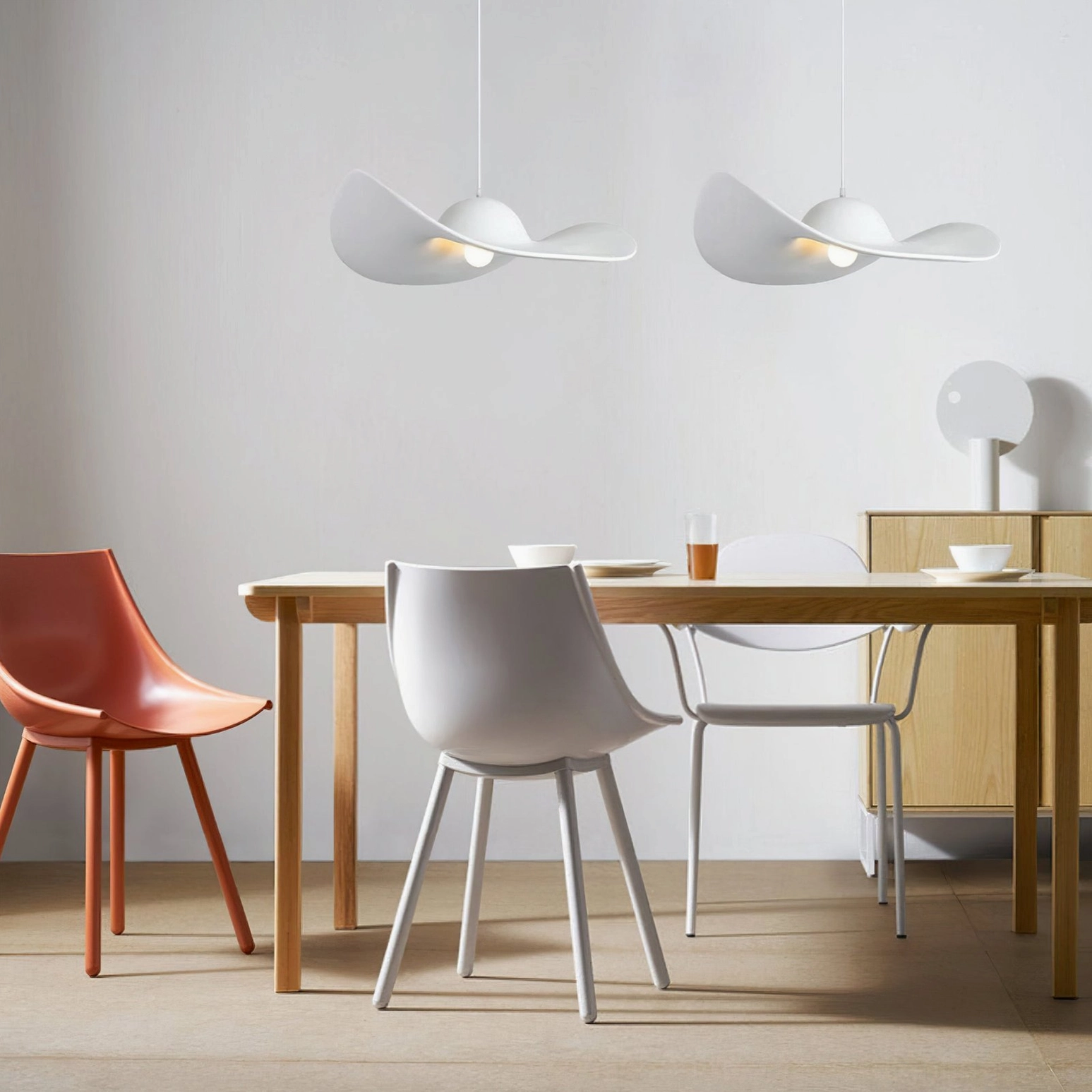 Two white hat pendant lights suspended over modern dining table with colorful chairs