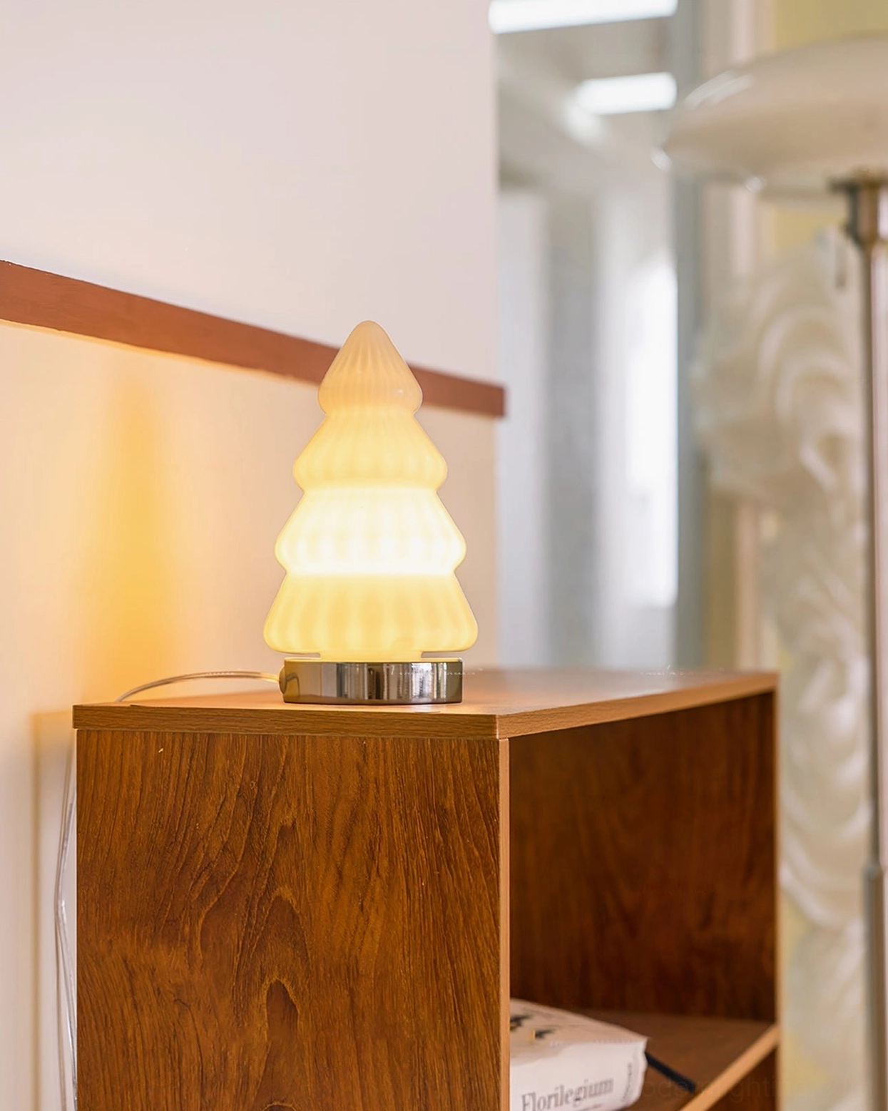 Lit white tree lamp on wooden shelf corner glowing with warm light showing ceramic ribbed shade and chrome base