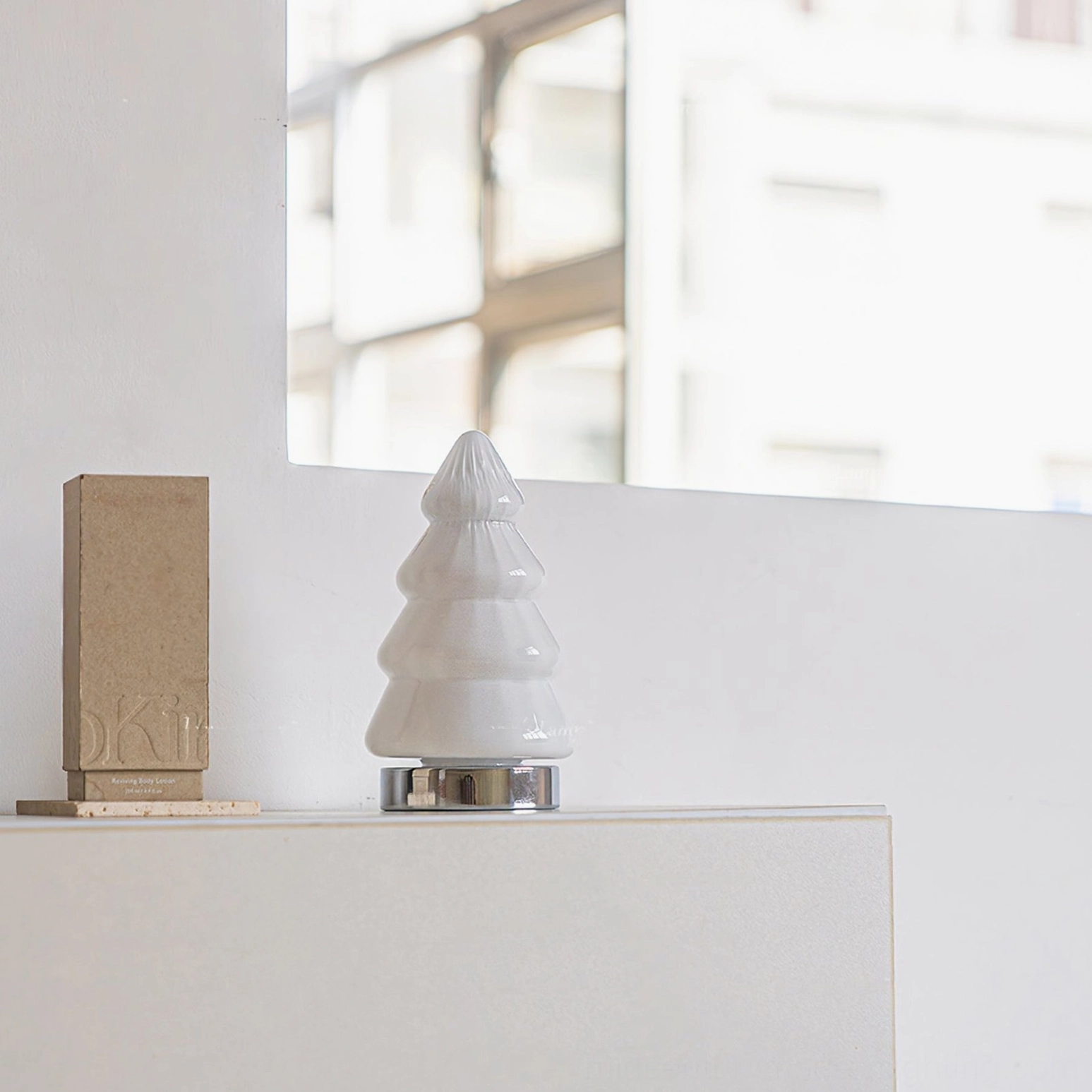Unlit white tree lamp on minimalist white countertop near window with concrete decor piece contemporary style