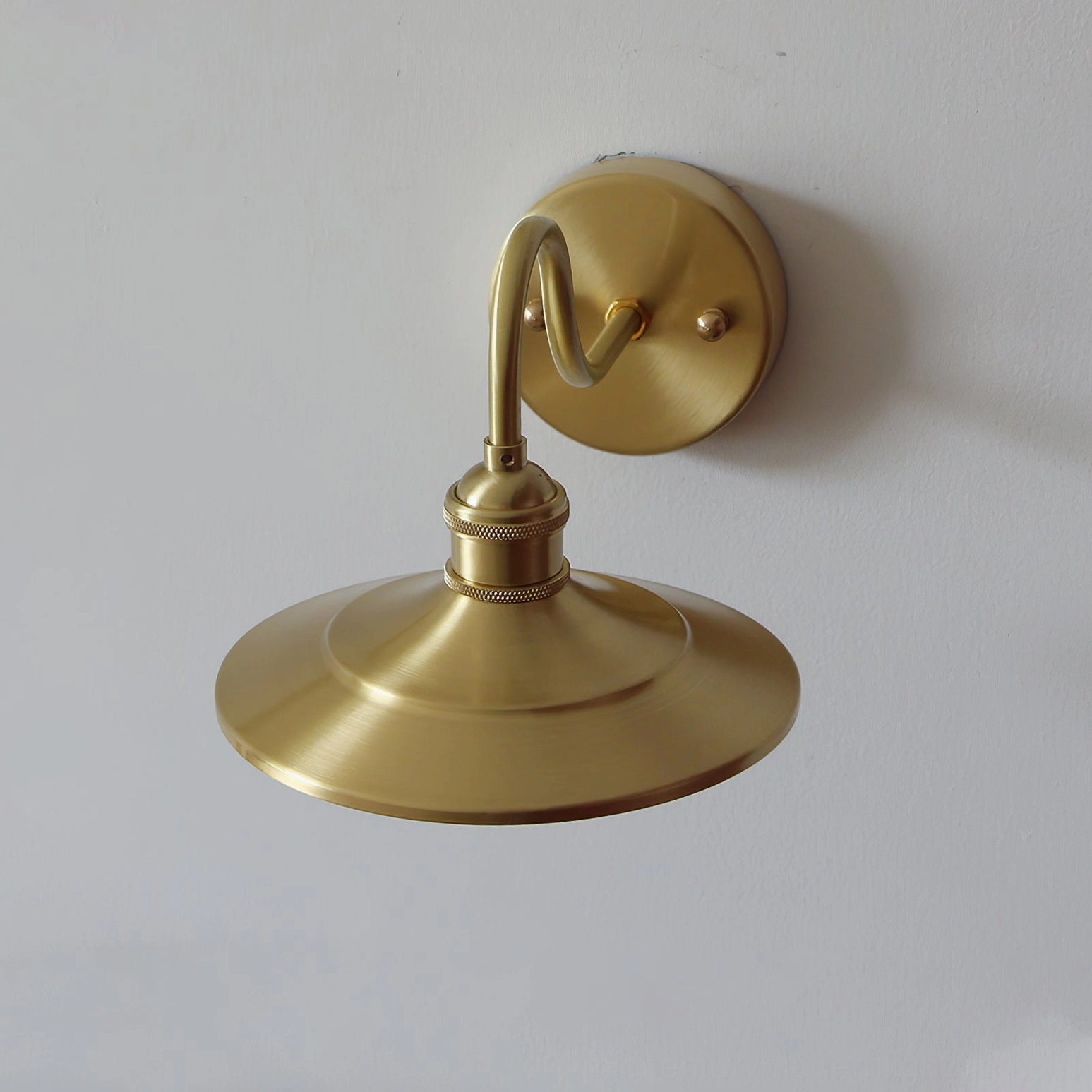 Large brass wall sconce Whizzer with conical shade and brushed metal texture detail on minimalist white wall