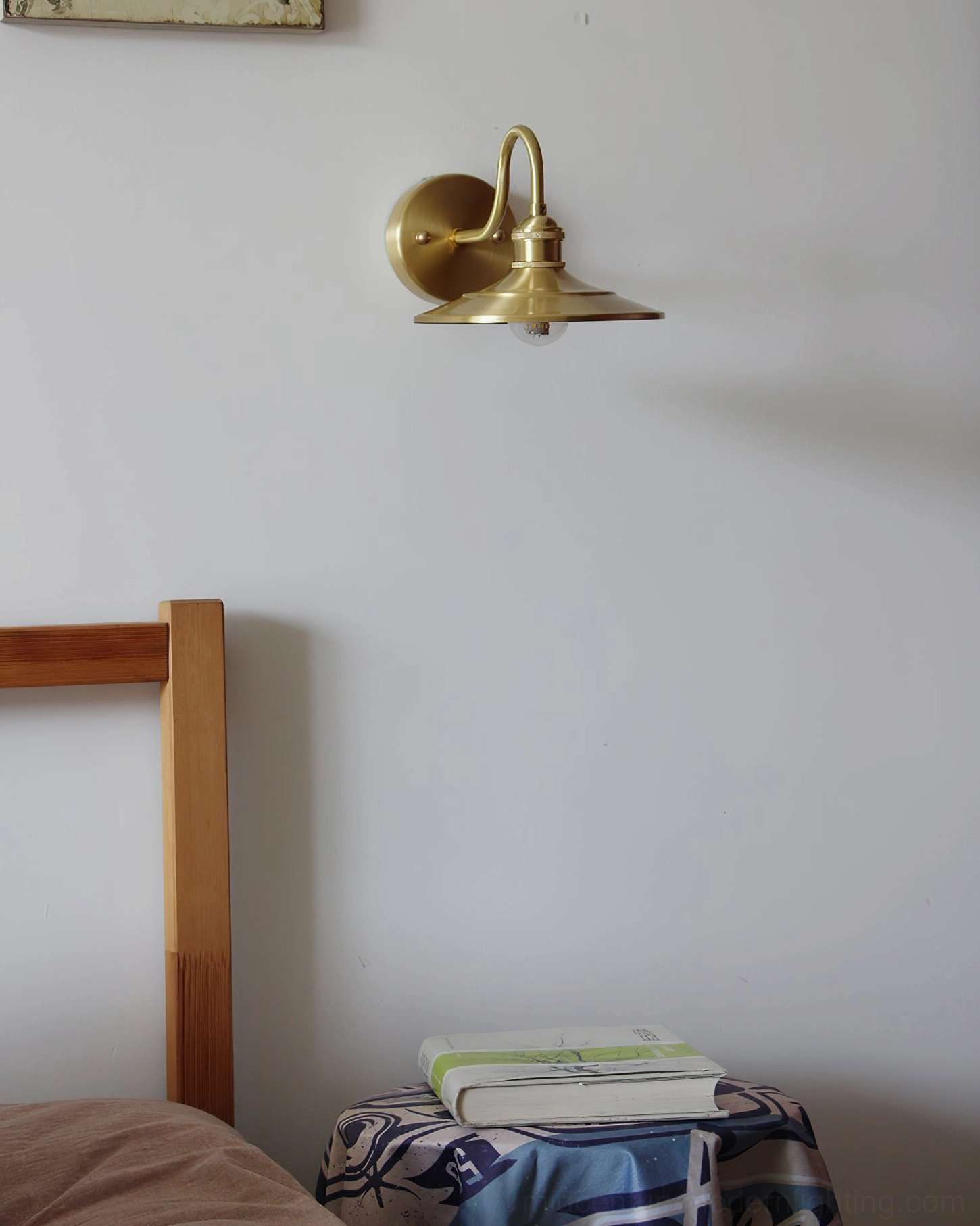 Whizzer wall-mounted brass lamp in bedroom space with patterned bedside fabric, wooden bed frame, and soft warm illumination