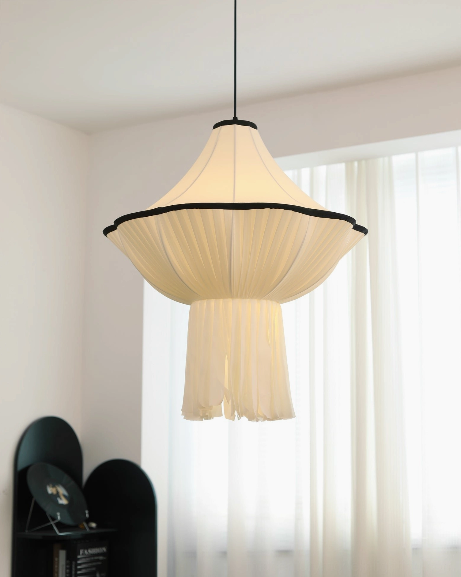 Wildon fabric pendant with wide flared pleated shade and black metal trim in bright interior space with sheer curtains