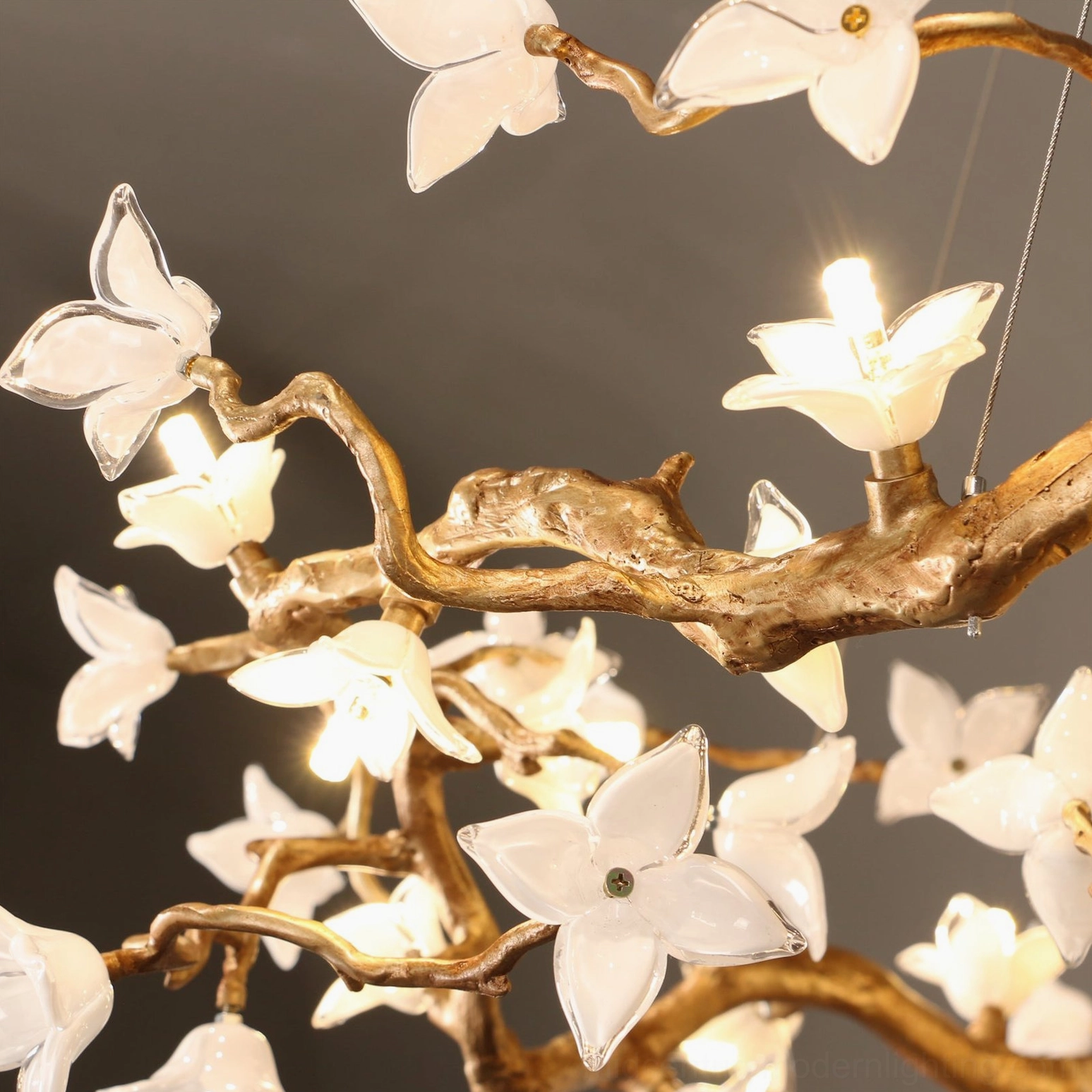 Willow Flower Chandelier low-angle close-up showing abundant glass flowers with warm glowing LED lights and intricate brass work