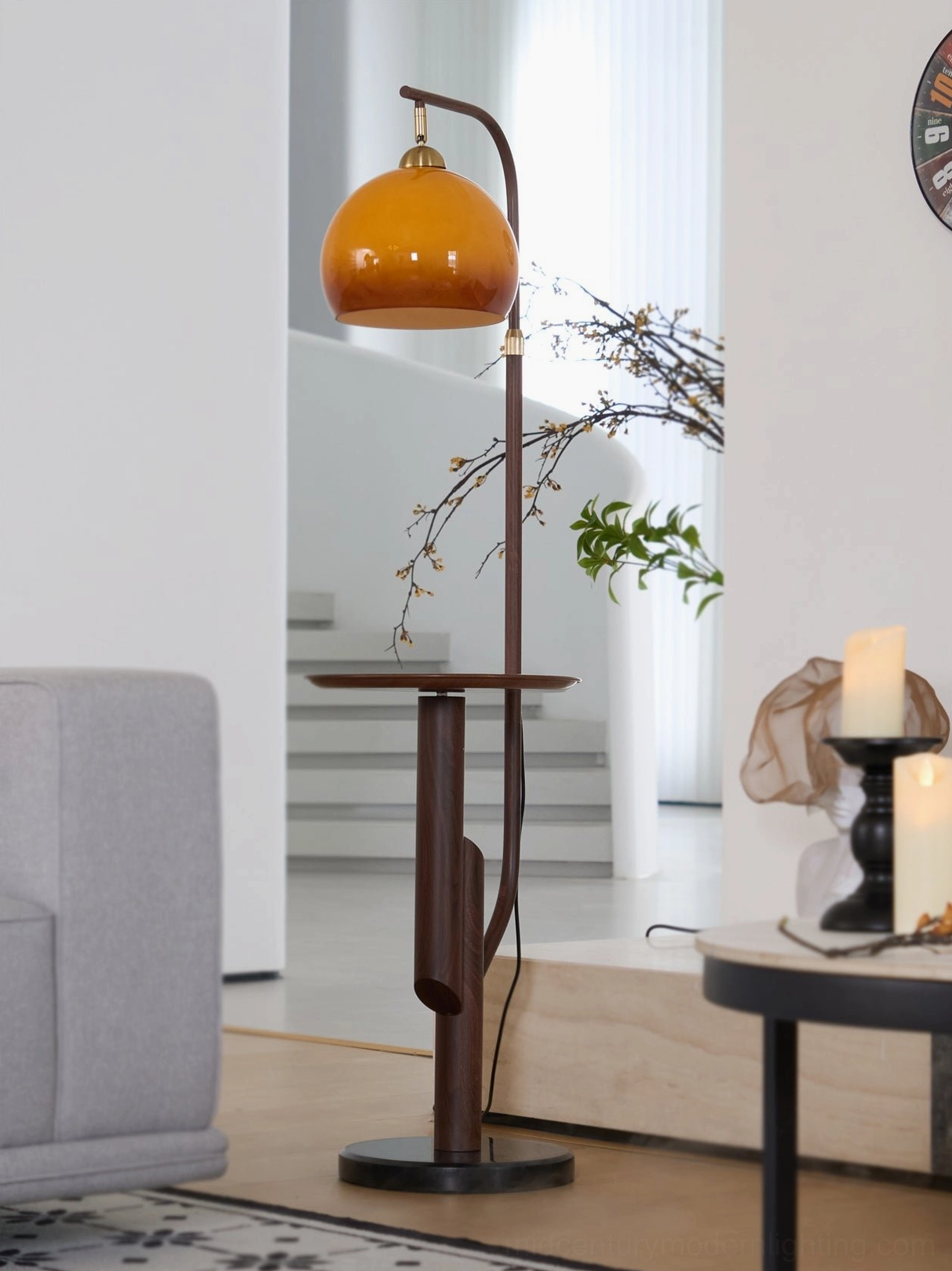 Winona arc floor lamp side profile with brown pole and amber glass lampshade, lit and positioned beside seating