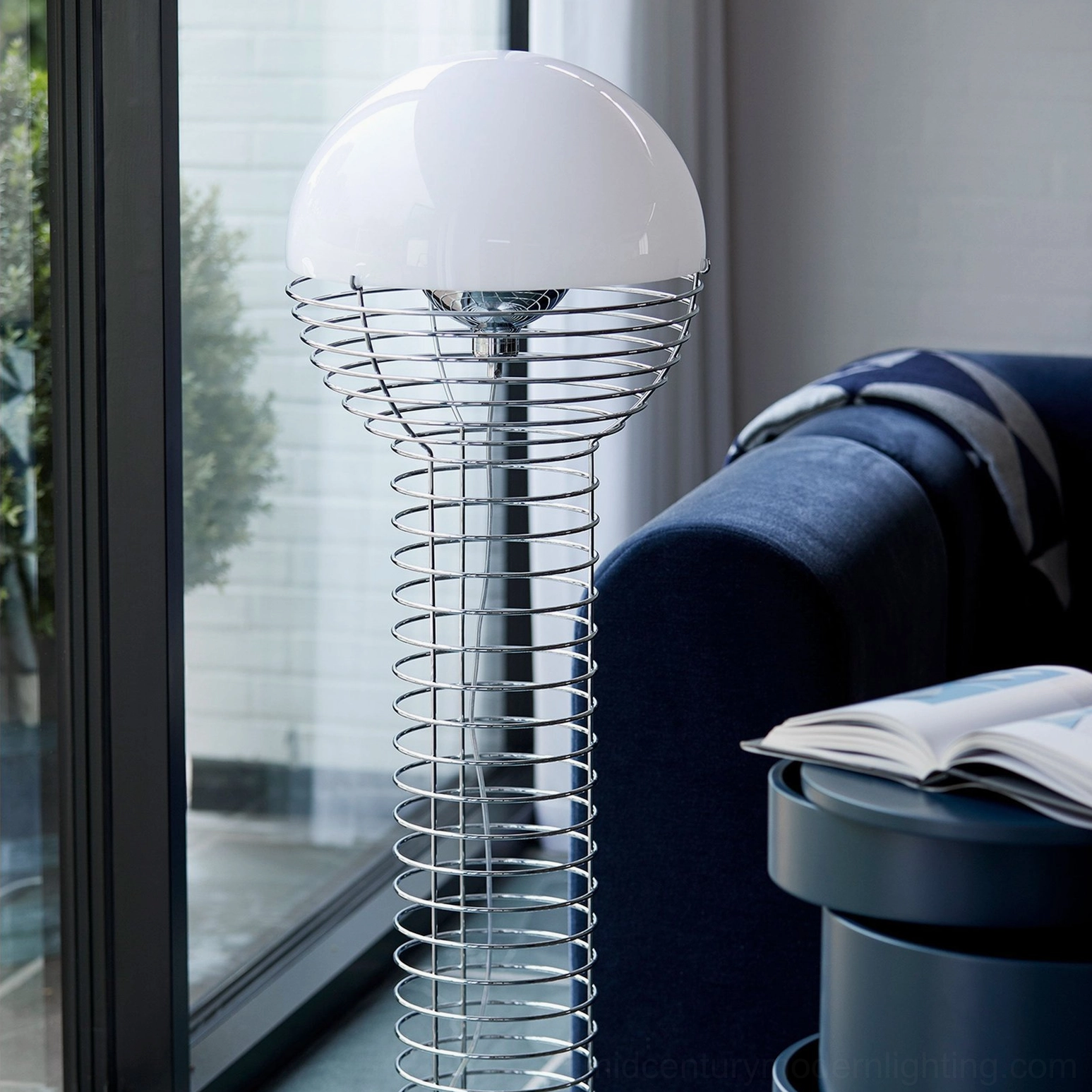 Wire floor lamp in home corner with dark blue sofa and natural daylight from large windows, mid-century style